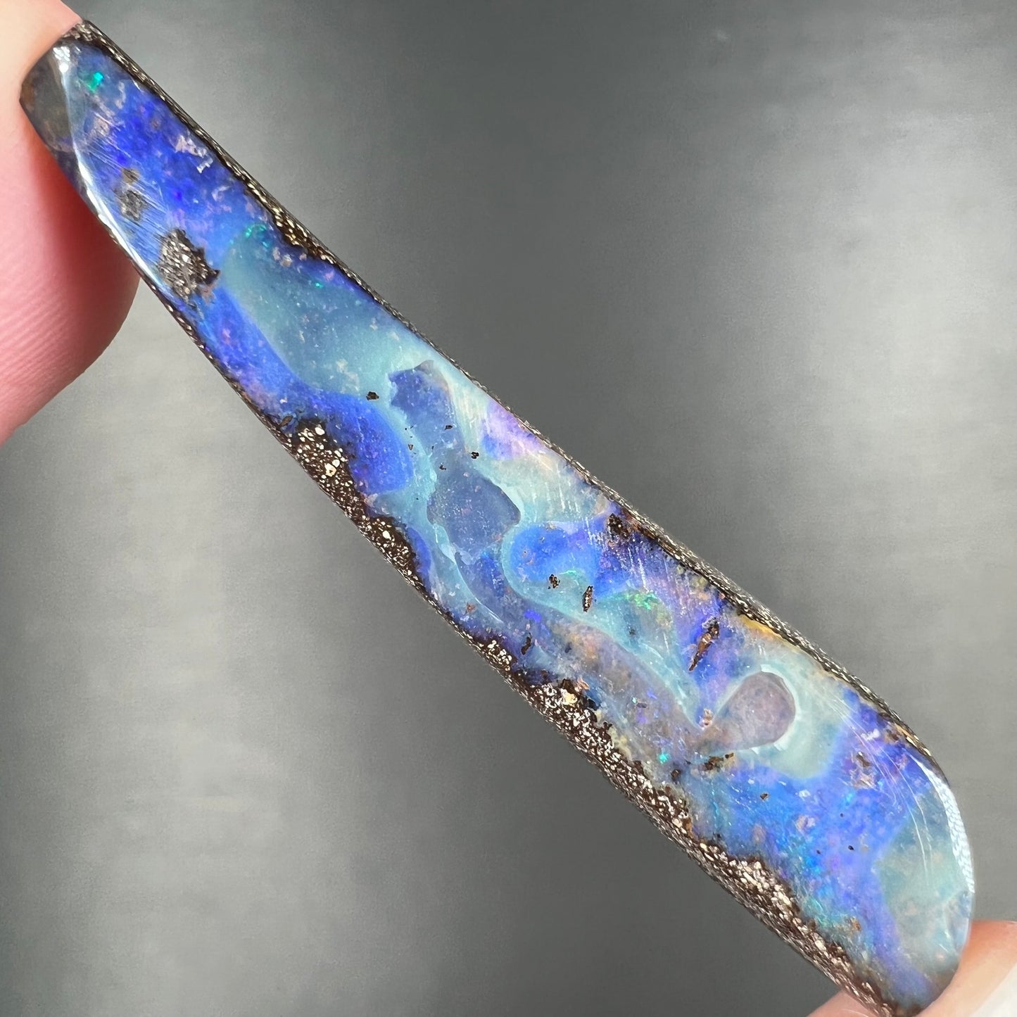 A loose, polished Quilpie boulder opal stone from Australia. The stone is predominantly blue.