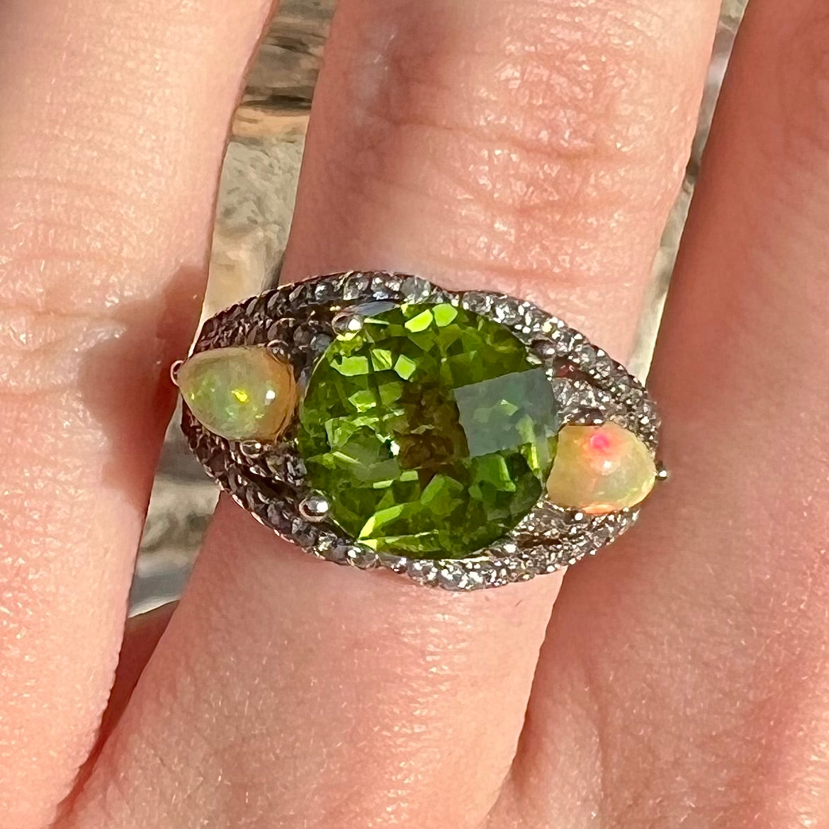 A sterling silver ring set with one large round peridot stone set between two pear shape cabochon Ethiopian opals. Cubic zirconia stones line the ring.