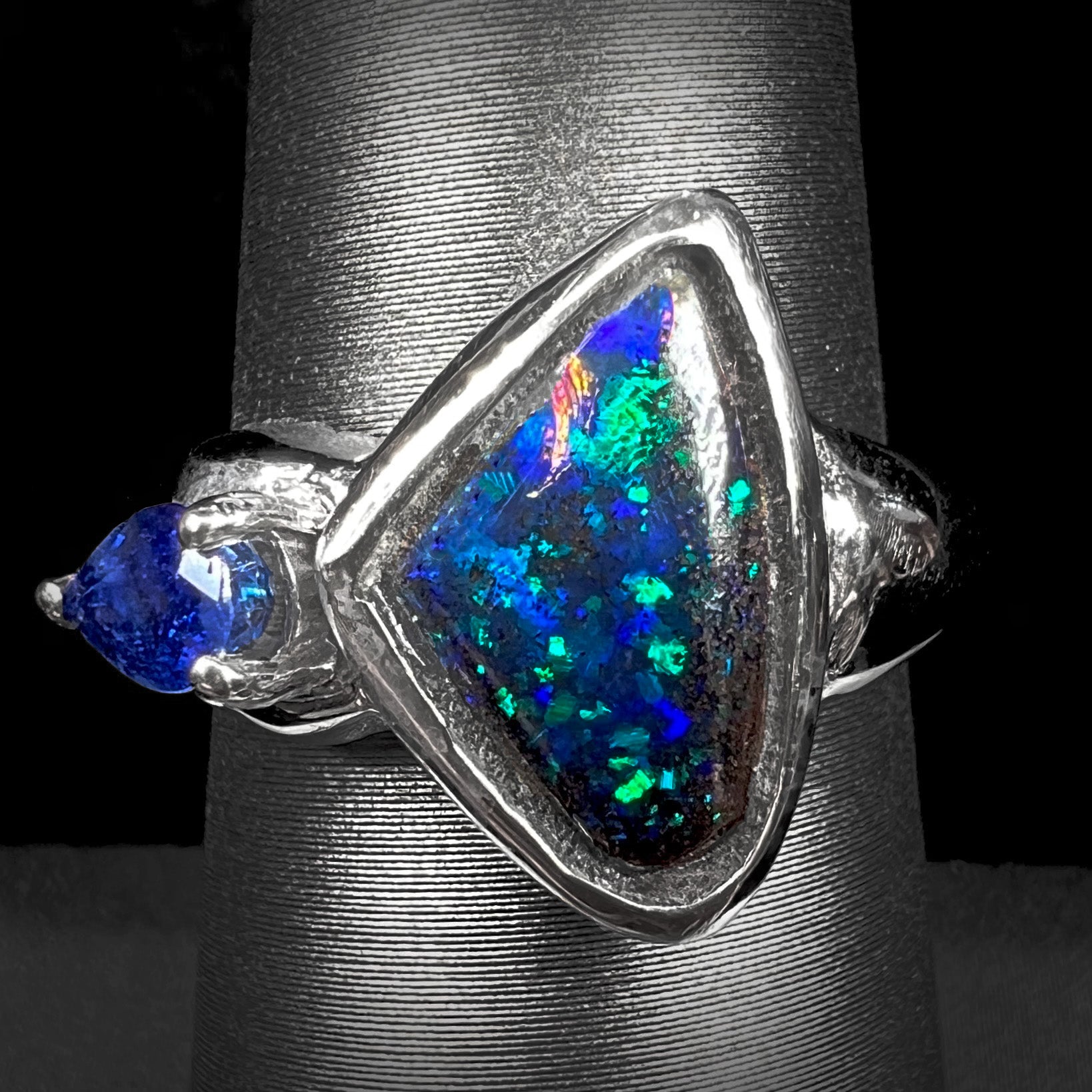 A ladies' white gold ring set with Australian black boulder opal and pear shape blue sapphire.