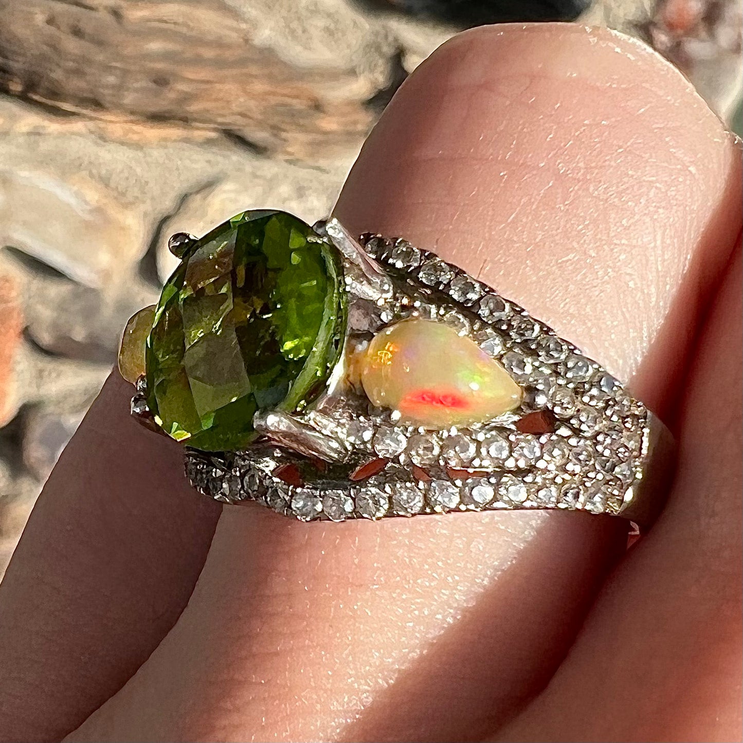 A sterling silver ring set with one large round peridot stone set between two pear shape cabochon Ethiopian opals. Cubic zirconia stones line the ring.