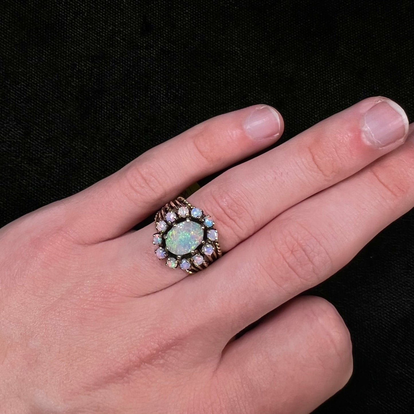 Vintage yellow gold oval opal cabochon ring set with 12 round opals in a halo around the center stone.