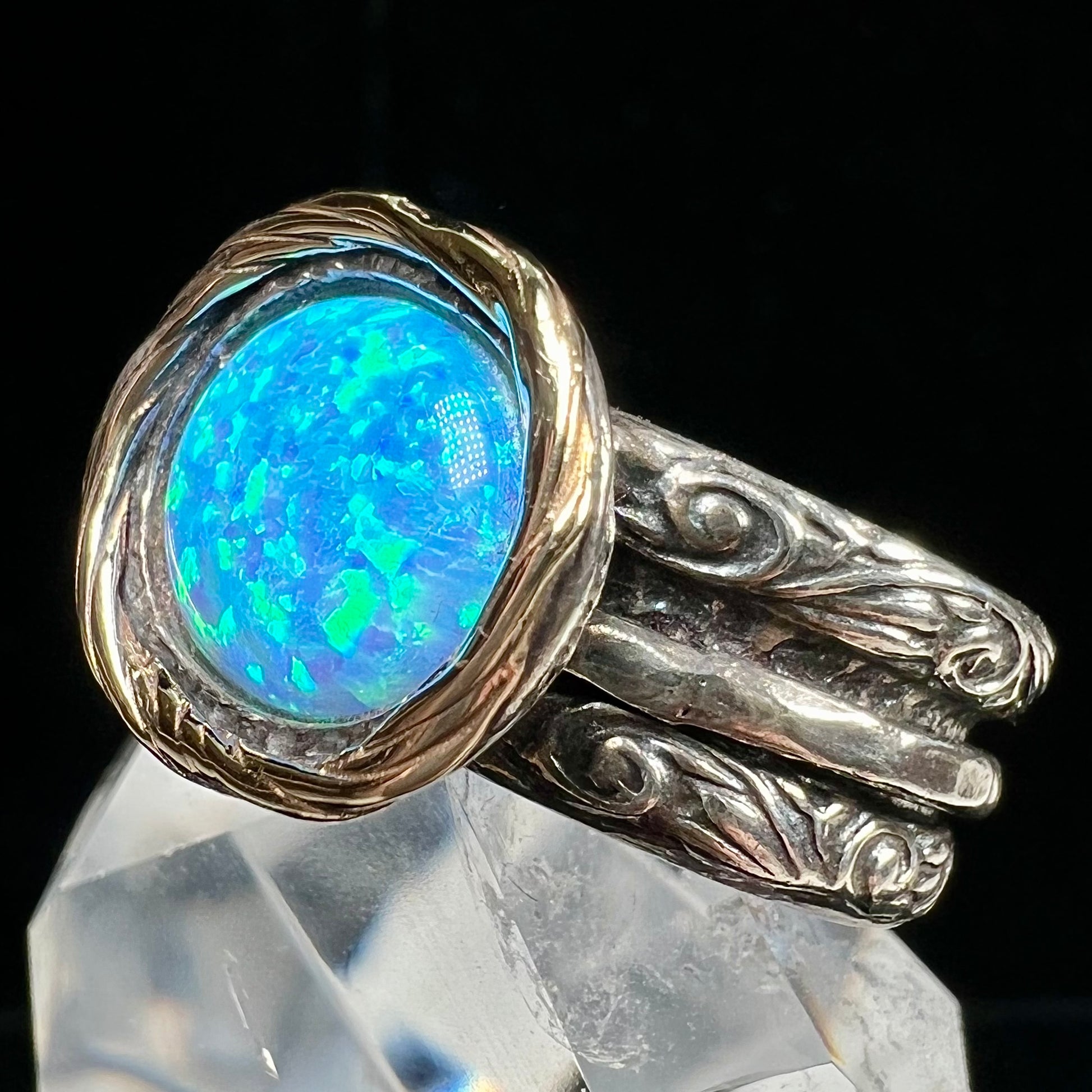 A filigree etched two tone silver and gold spinner ring set with a lab created black opal.