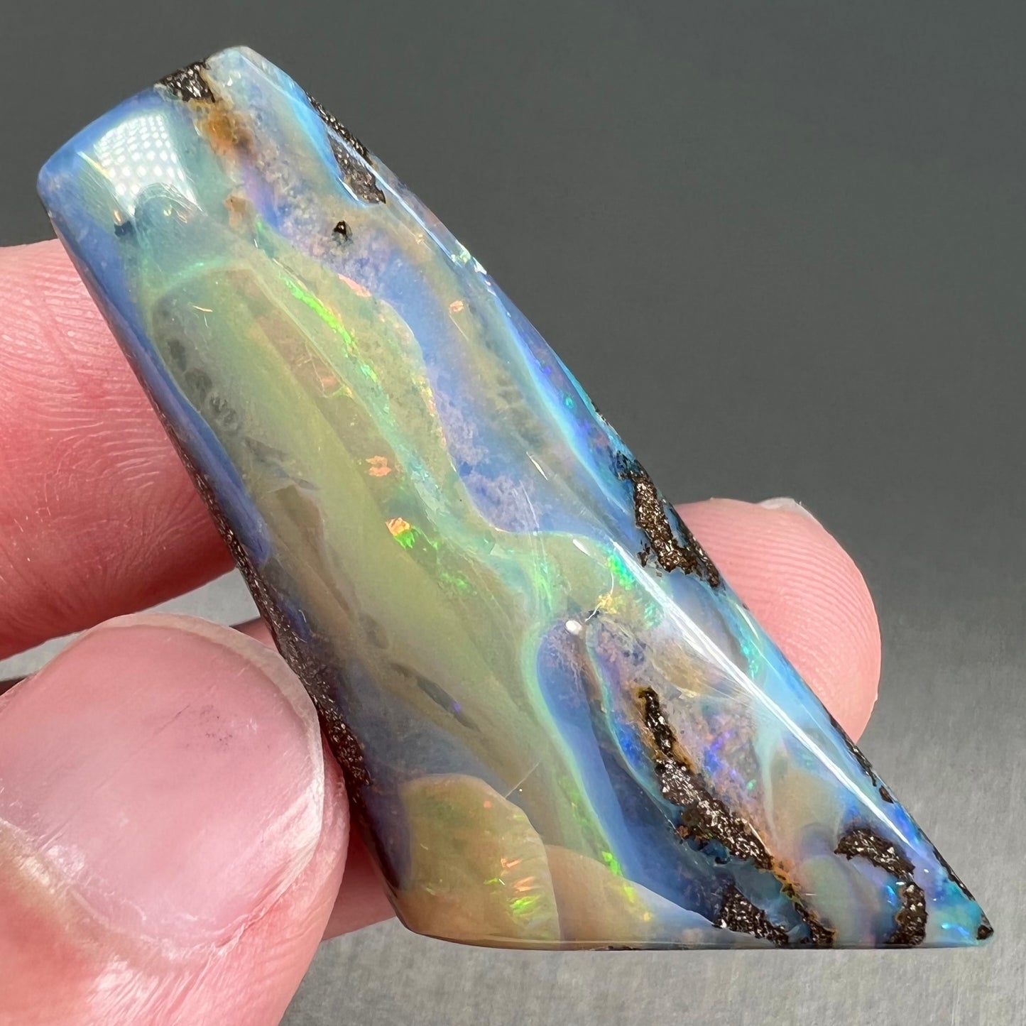 A freeform shaped, polished boulder opal stone from Queensland, Australia. The stone has red, orange, green, and blue fire.