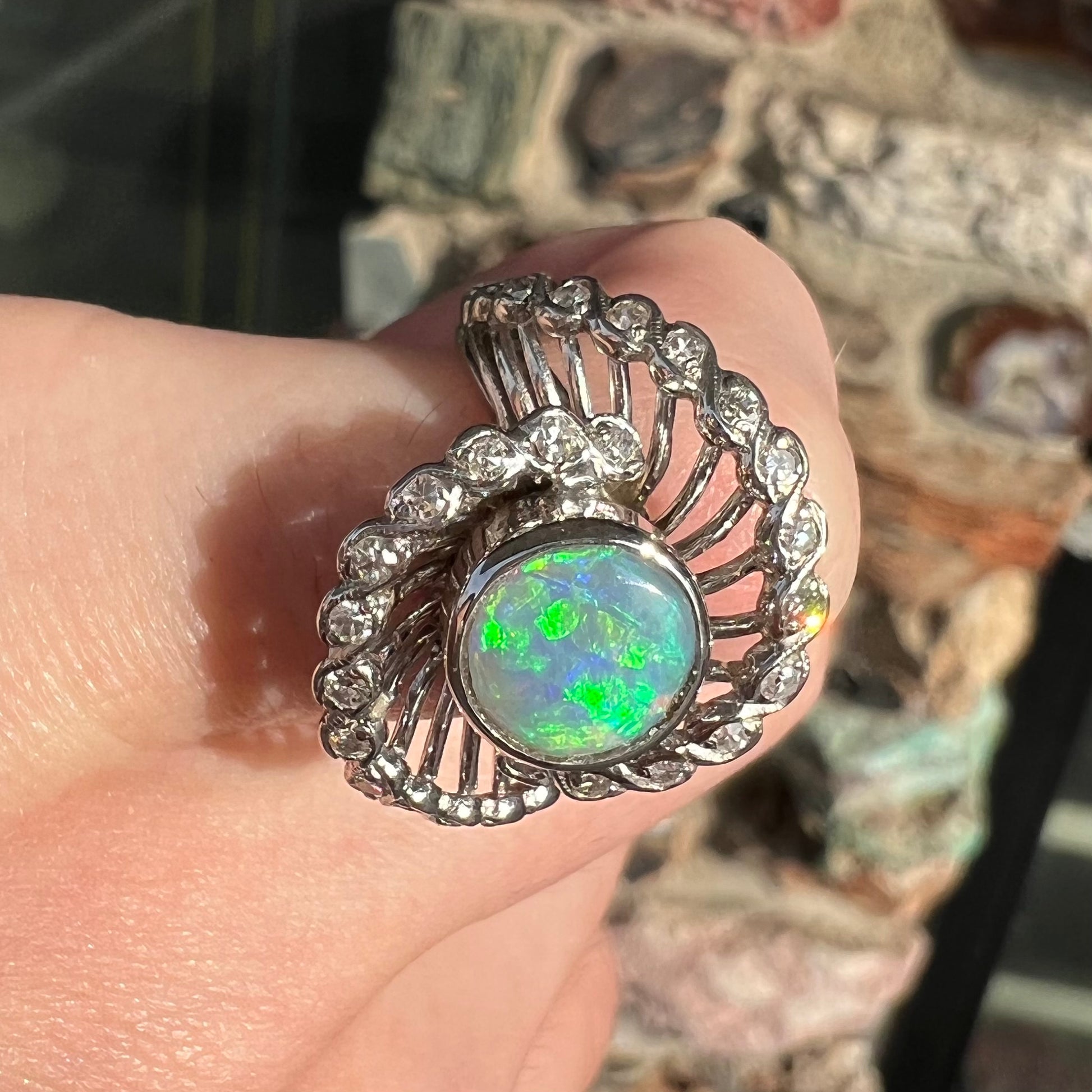 A white gold ring featuring a round cabochon cut black opal set in a swirl of round cut diamonds.