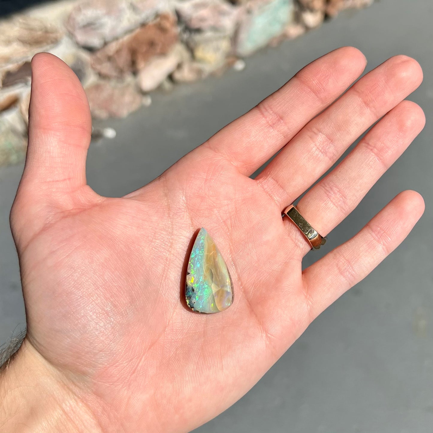 A loose, pear shaped boulder opal stone from Queensland, Australia. Predominant colors are blue, purple, and green.