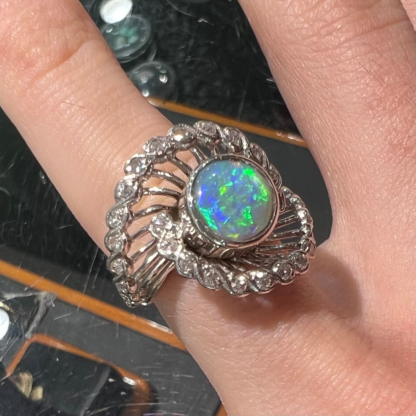 A white gold ring featuring a round cabochon cut black opal set in a swirl of round cut diamonds.