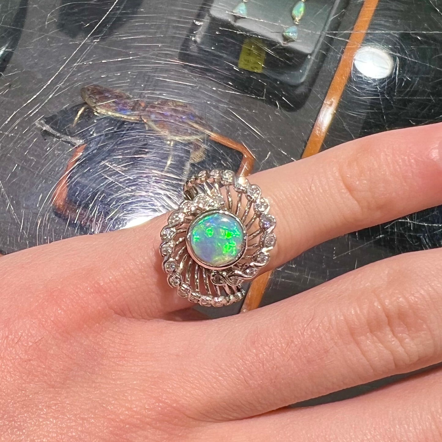 A white gold ring featuring a round cabochon cut black opal set in a swirl of round cut diamonds.