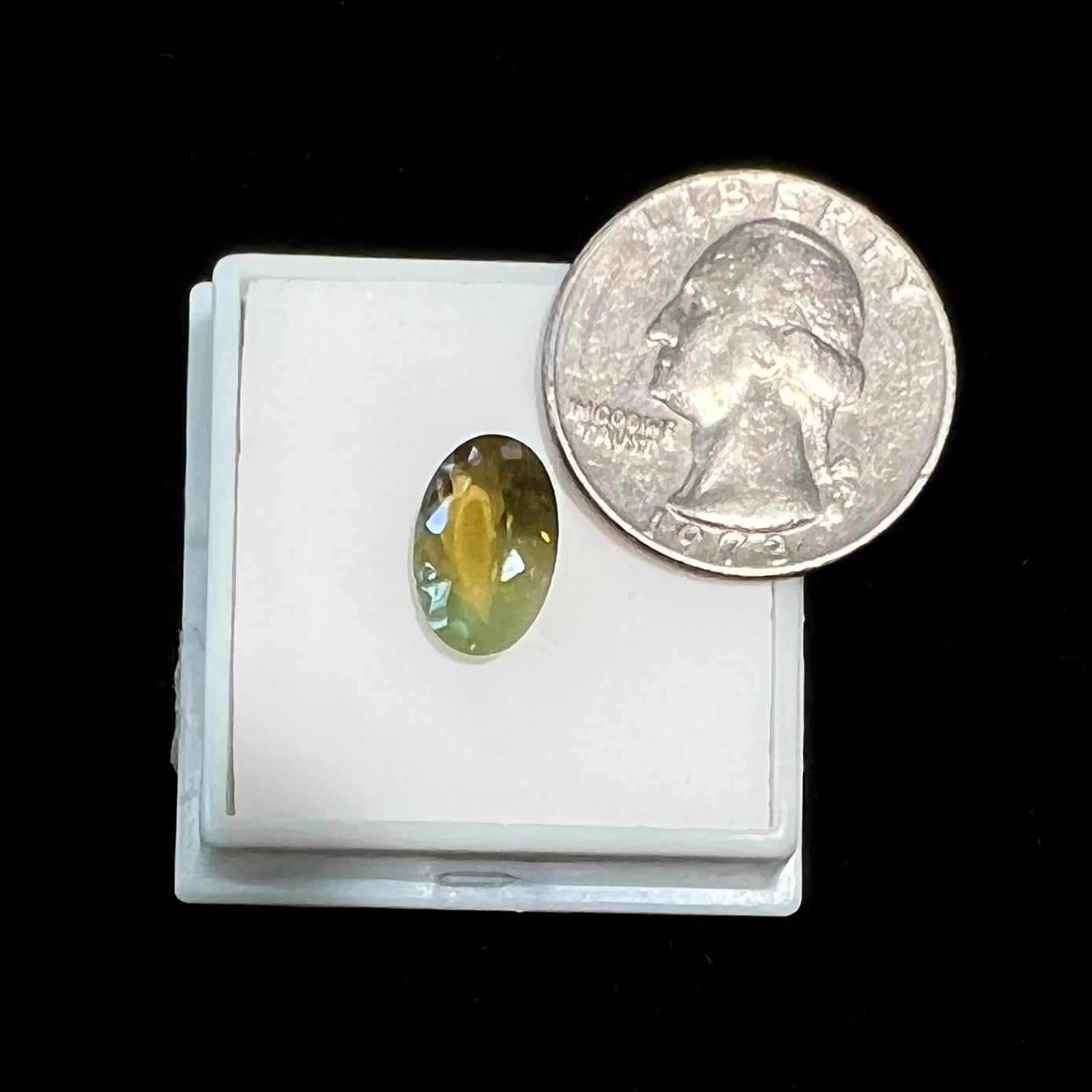 A loose, faceted oval cut bicolor chrysoberyl stone. The stone goes from neon green to dark green with orangey red flashes.