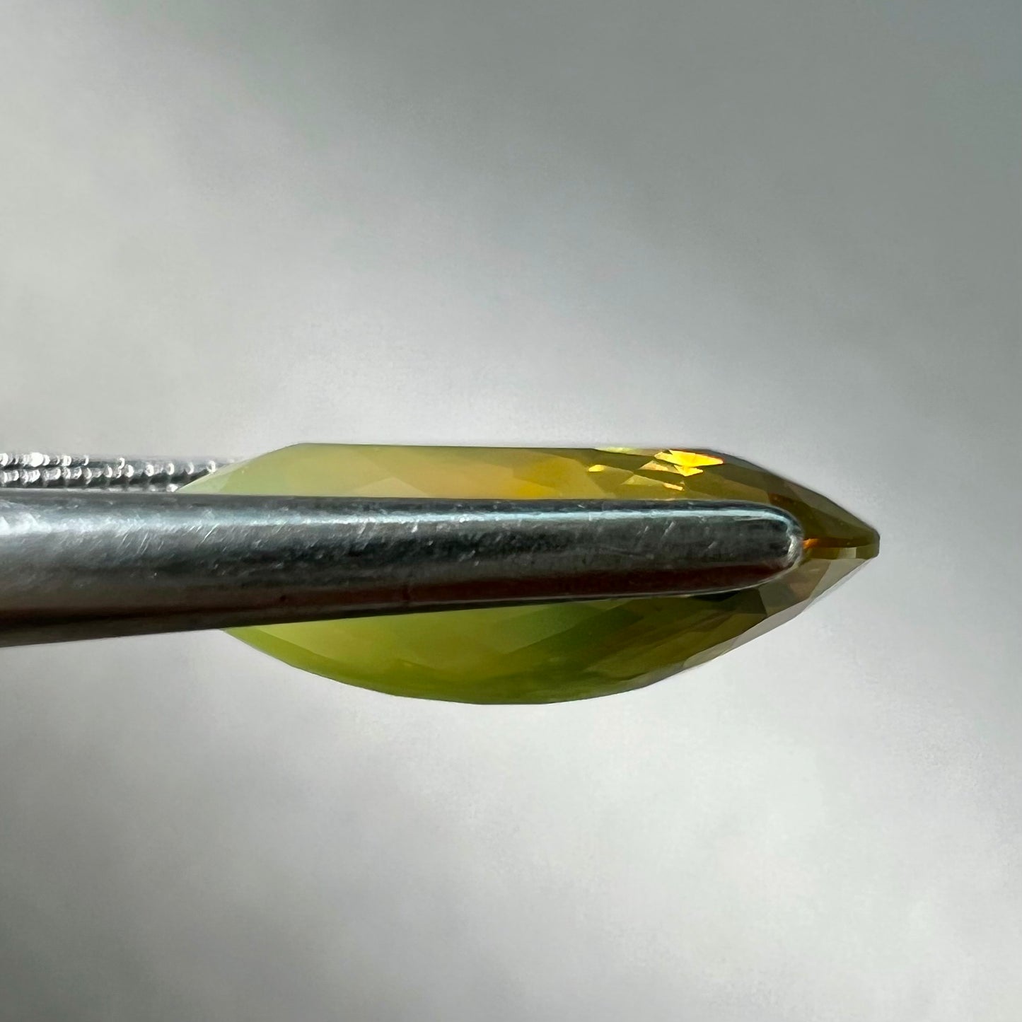 A loose, faceted oval cut bicolor chrysoberyl stone. The stone goes from neon green to dark green with orangey red flashes.