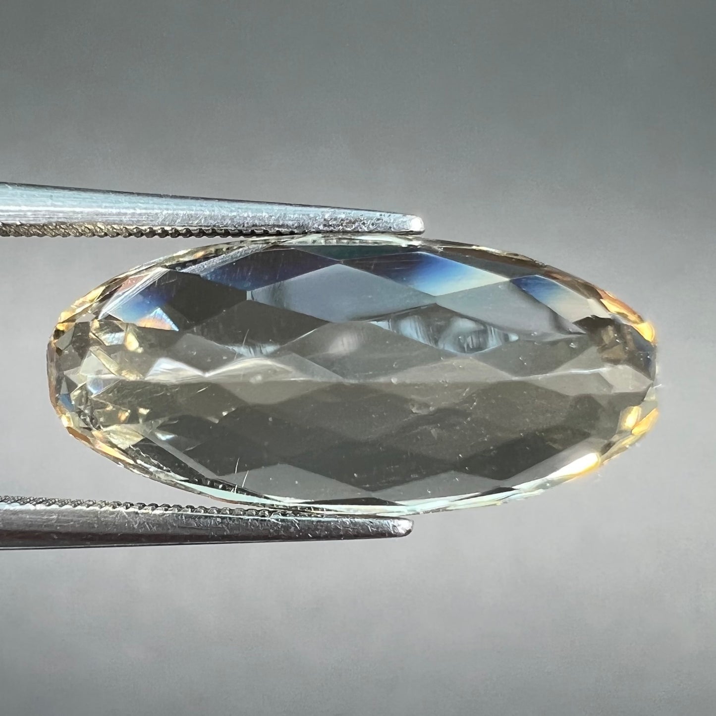A loose, oval cut golden topaz gemstone. A stronger concentration of yellow rests in the edges of the stone.