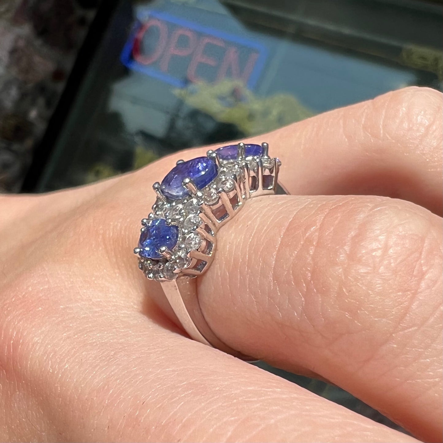 A sterling silver past, present, future three stone tanzanite ring. The main stones are set in a halo of cubic zirconia.