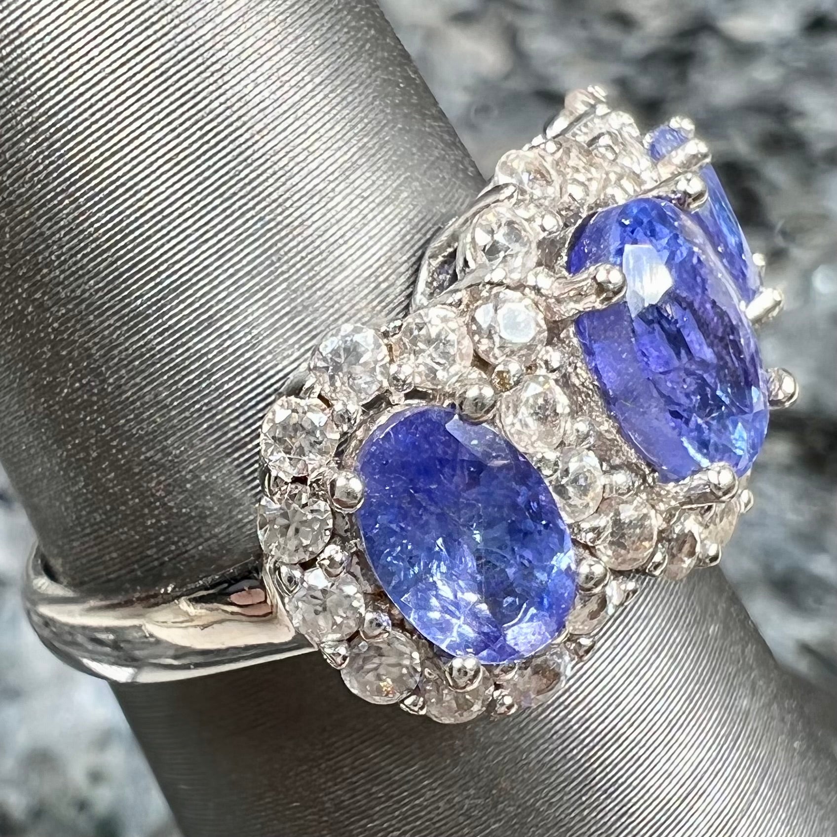 A sterling silver past, present, future three stone tanzanite ring.  The main stones are set in a halo of cubic zirconia.
