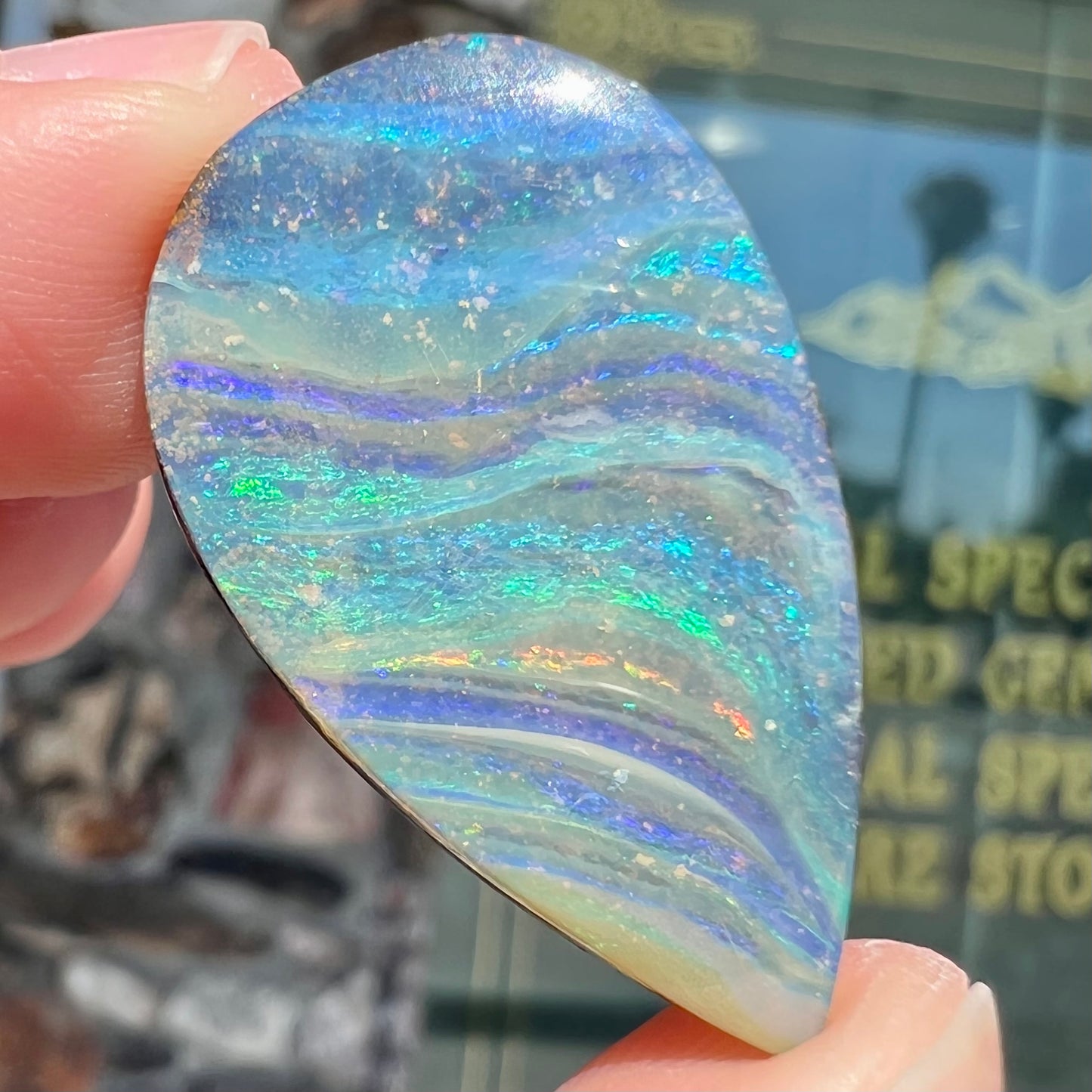 A loose, pear shaped boulder opal stone from Quilpie, Australia. The stone is predominantly blue, green, and purple with red and orange undertones.