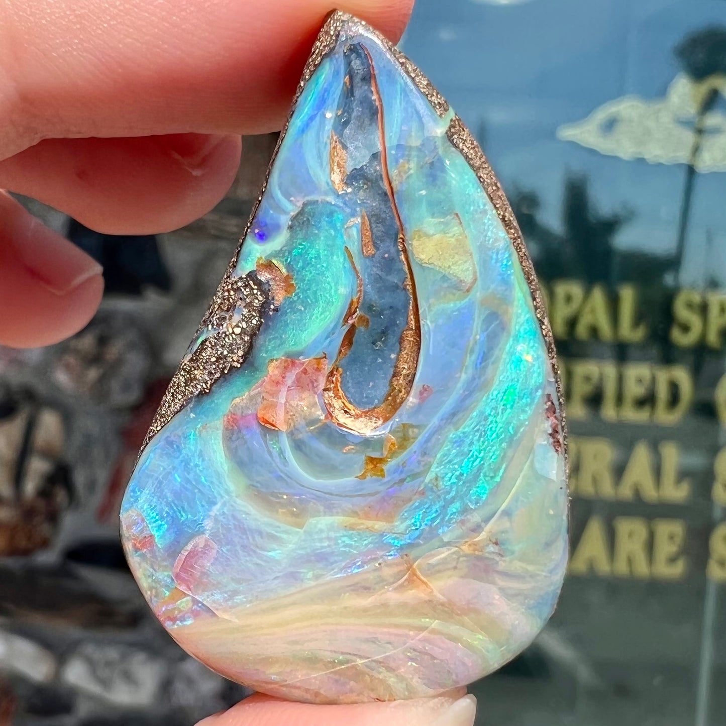 A polished pear shaped boulder opal stone from Quilpie, Australia. Predominant colors are blue, green, and aqua.