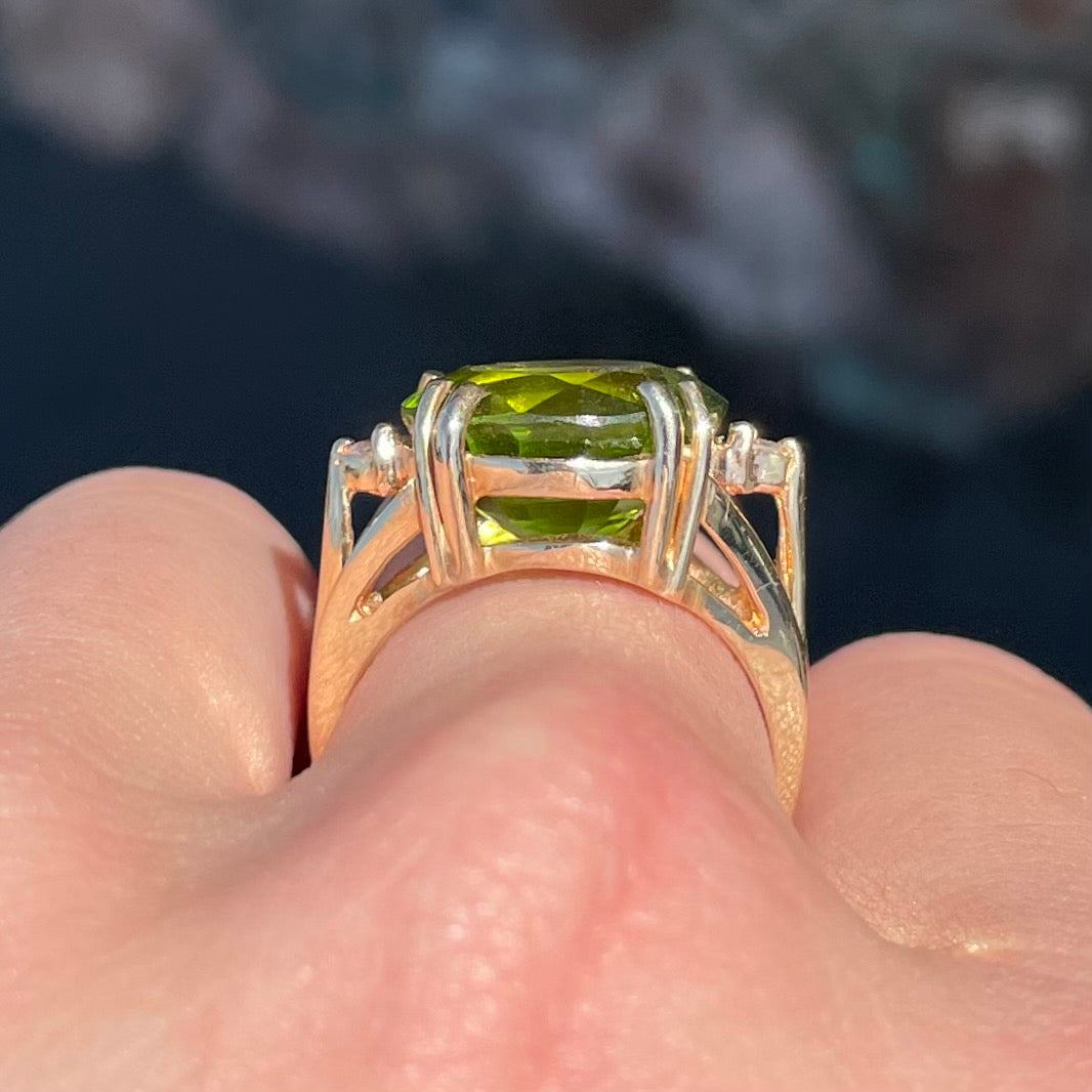 A ladies' round brilliant cut peridot statement ring set with two round diamond accents in yellow gold.