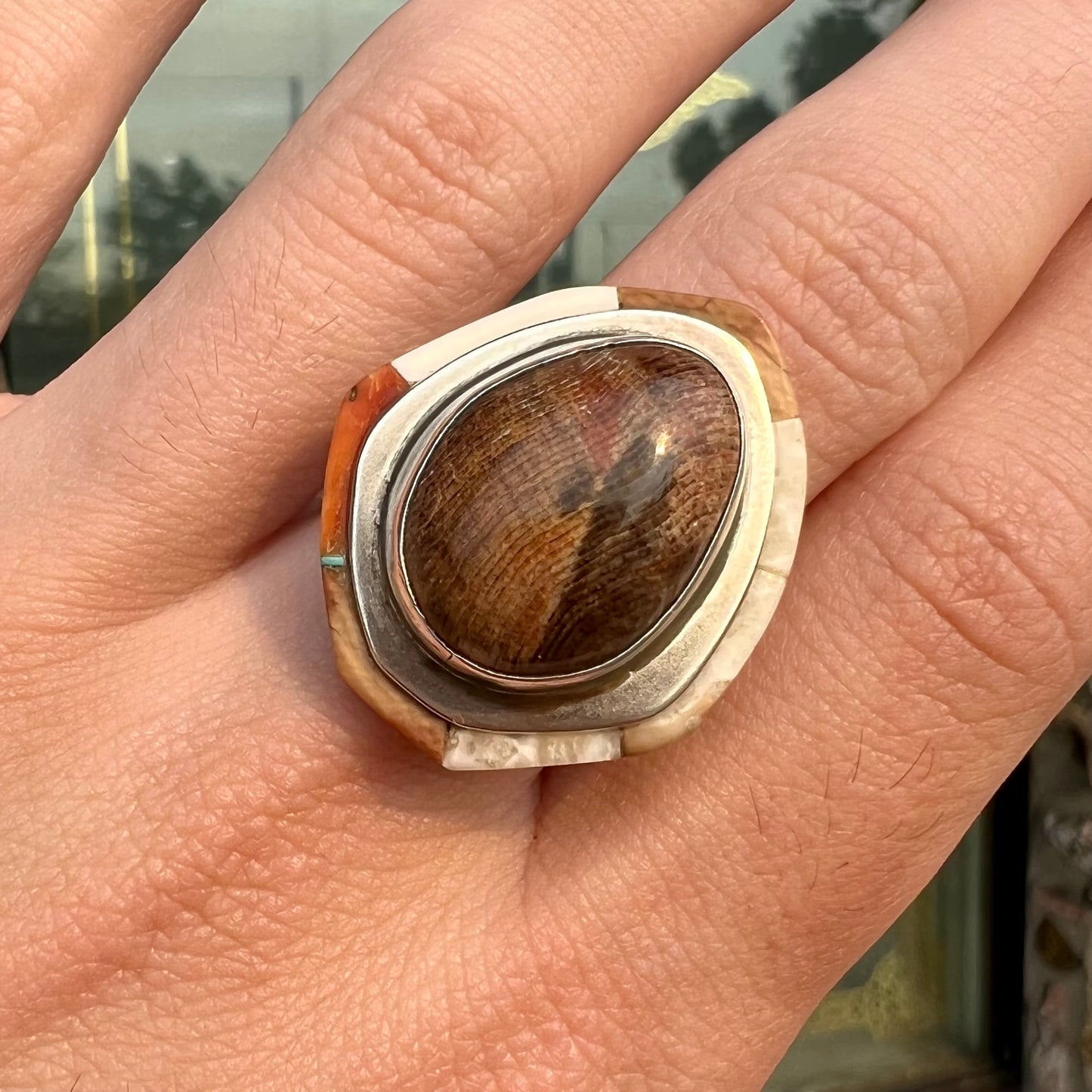 A silver ring handmade from a bezel set petrified wood stone, surrounded by quartz, carnelian, and bone inlay.