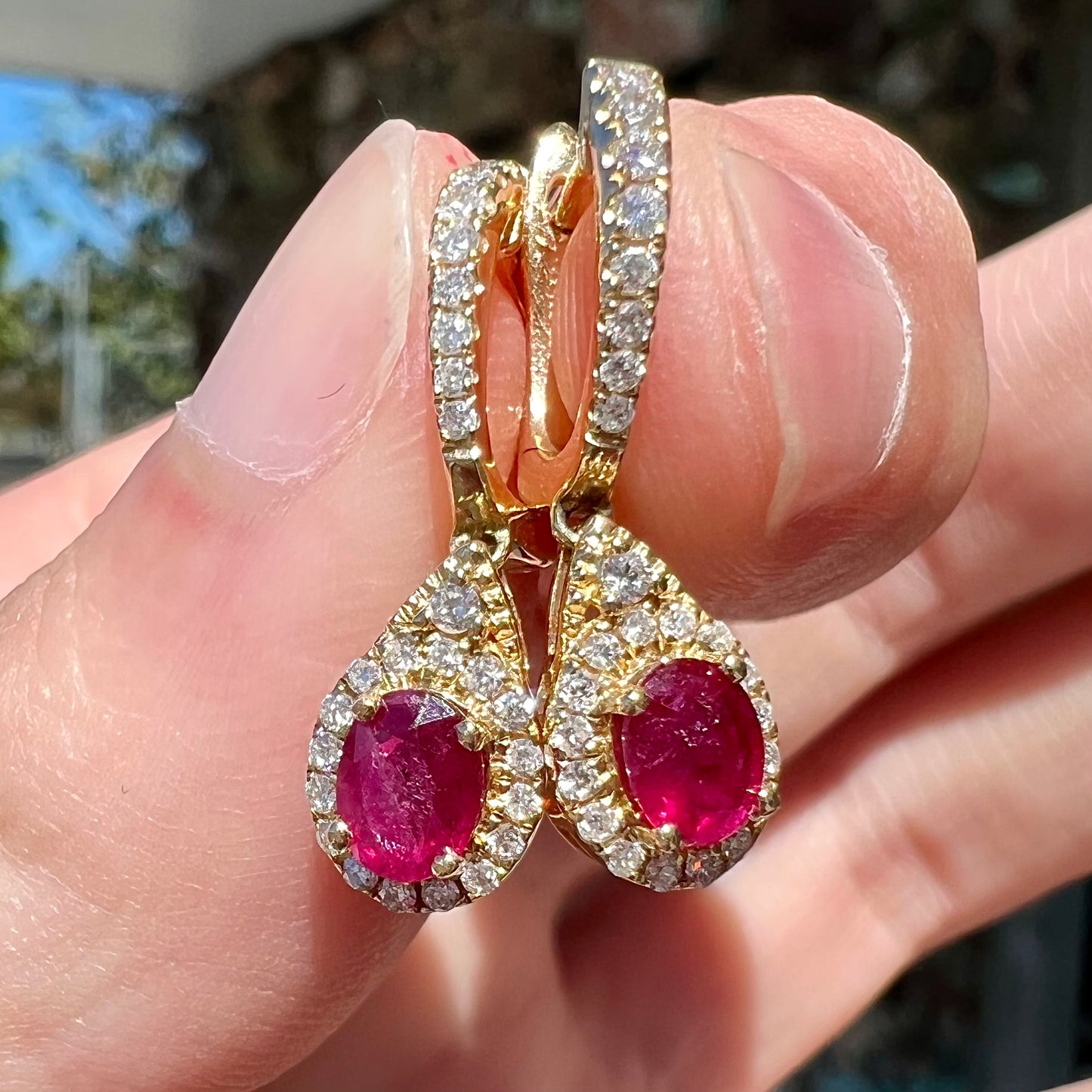 A pair of ruby and diamod halo dangle earrings cast in 14k yellow gold.