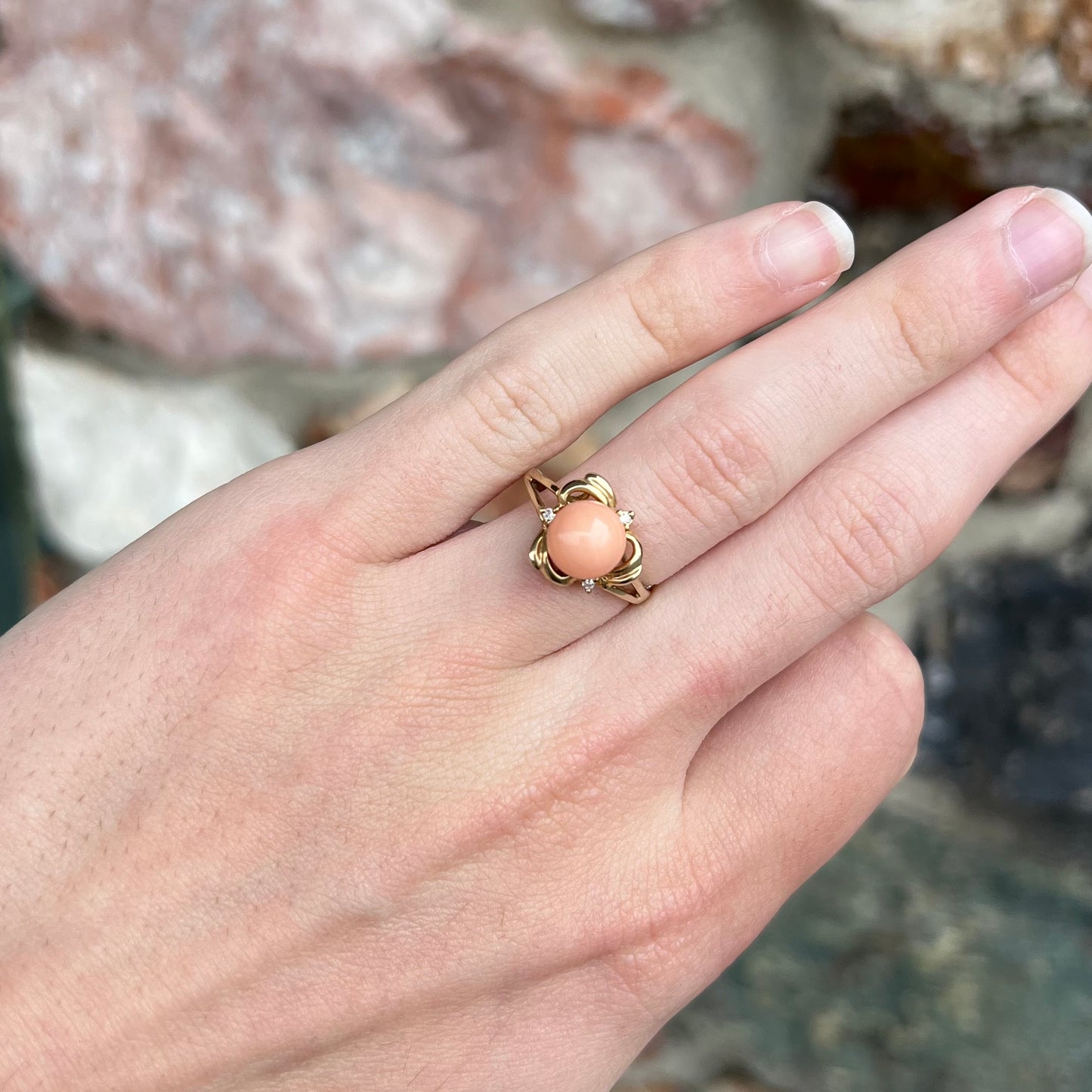 A vintage split shank flower ring set with a round pink coral sphere and diamond accents.