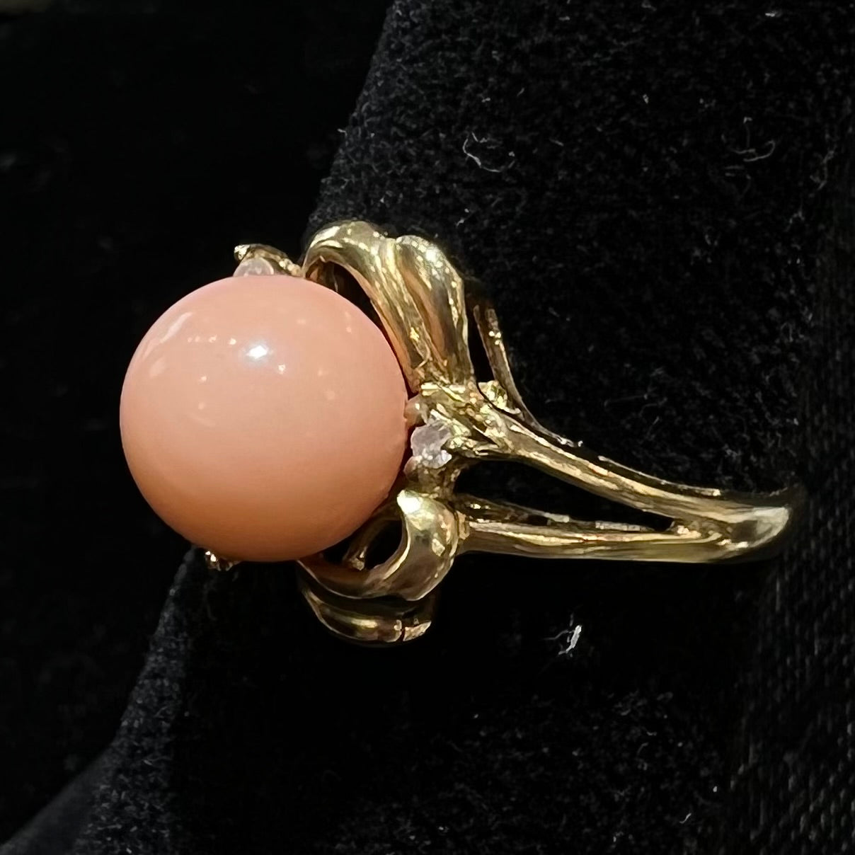 A vintage split shank flower ring set with a round pink coral sphere and diamond accents.