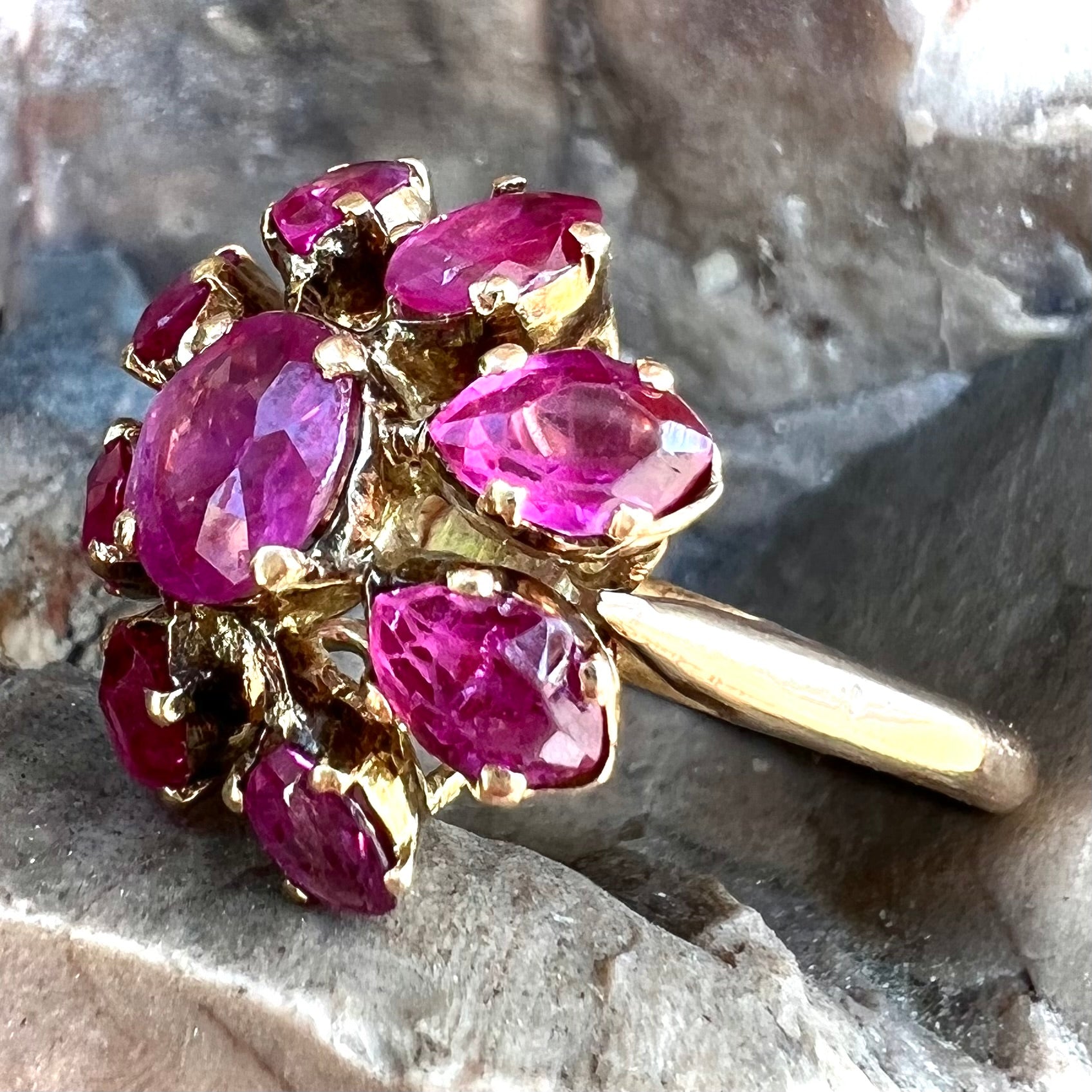 A yellow gold pink Burma ruby cluster ring with a faceted oval center stone surrounded by marquise cut stones.