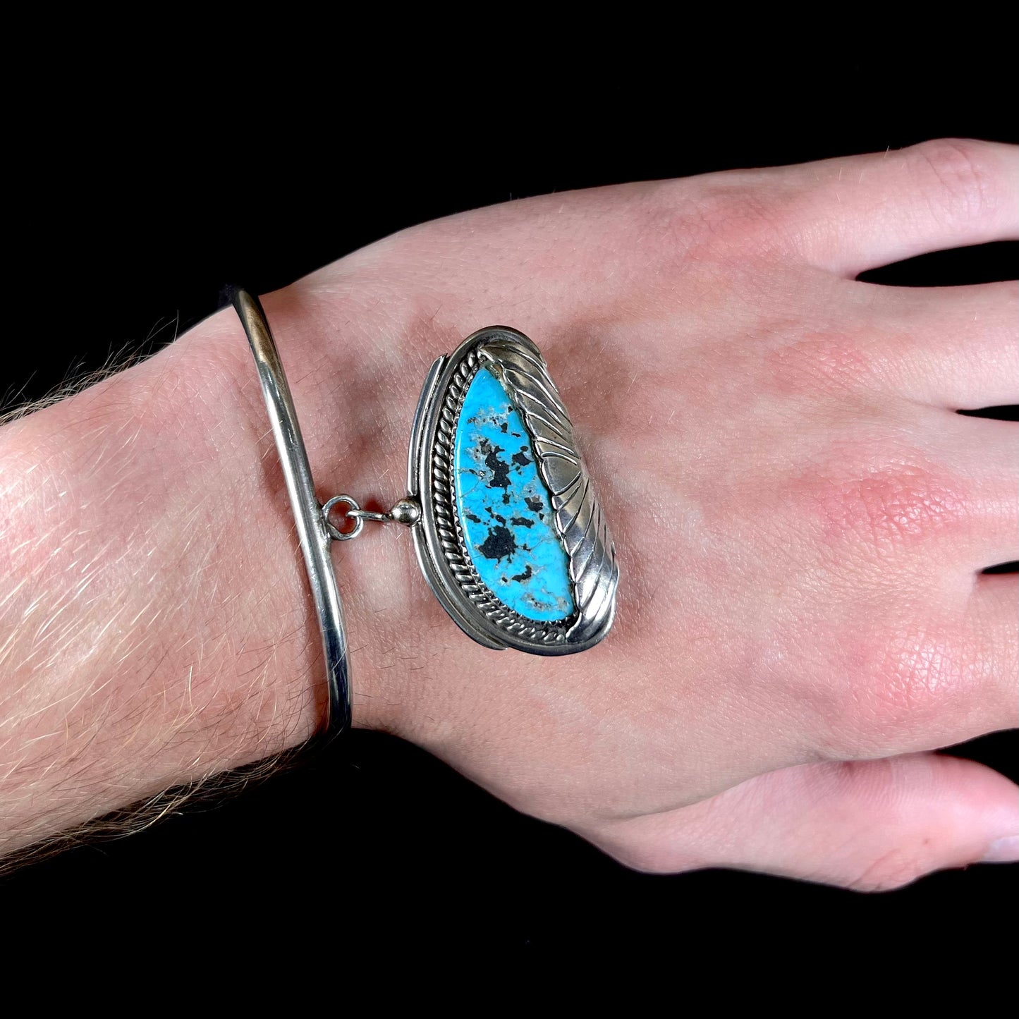 A sterling silver cuff bracelet with an attached dangle segment set with a turquoise stone from Pinto Valley.