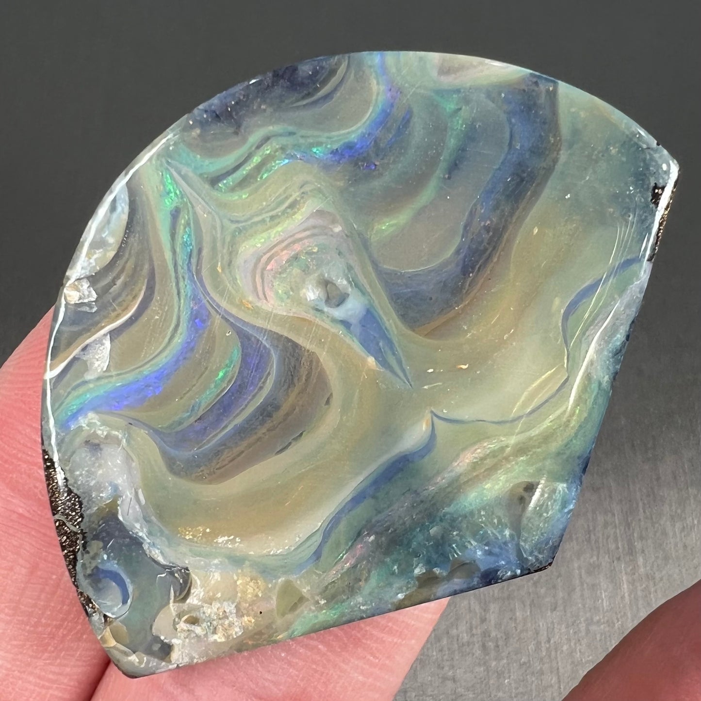 A polished, loose boulder opal stone from Queensland, Australia. Fire colors are green, blue, purple, and salmon.