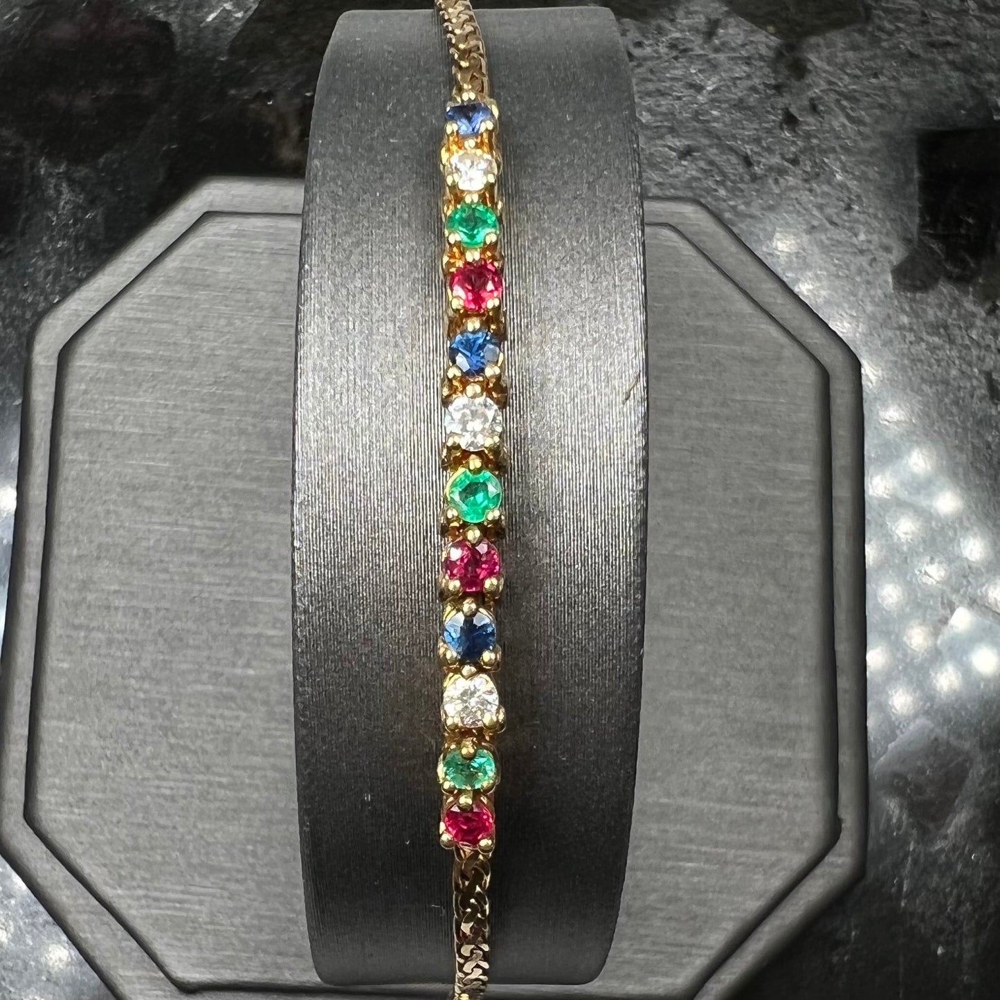 An 18k yellow gold bracelet set with natural rubies, sapphires, diamonds, and emeralds.