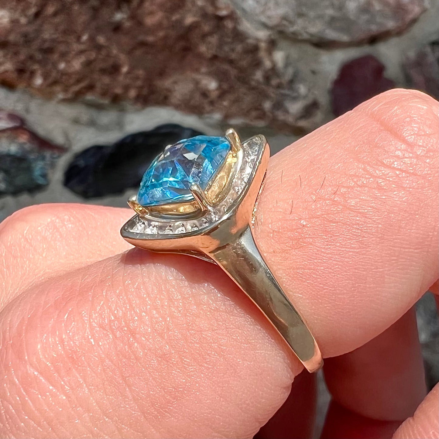 A checkerboard princess cut Swiss blue topaz ring. The stone is set in a yellow gold, diamond halo mounting.