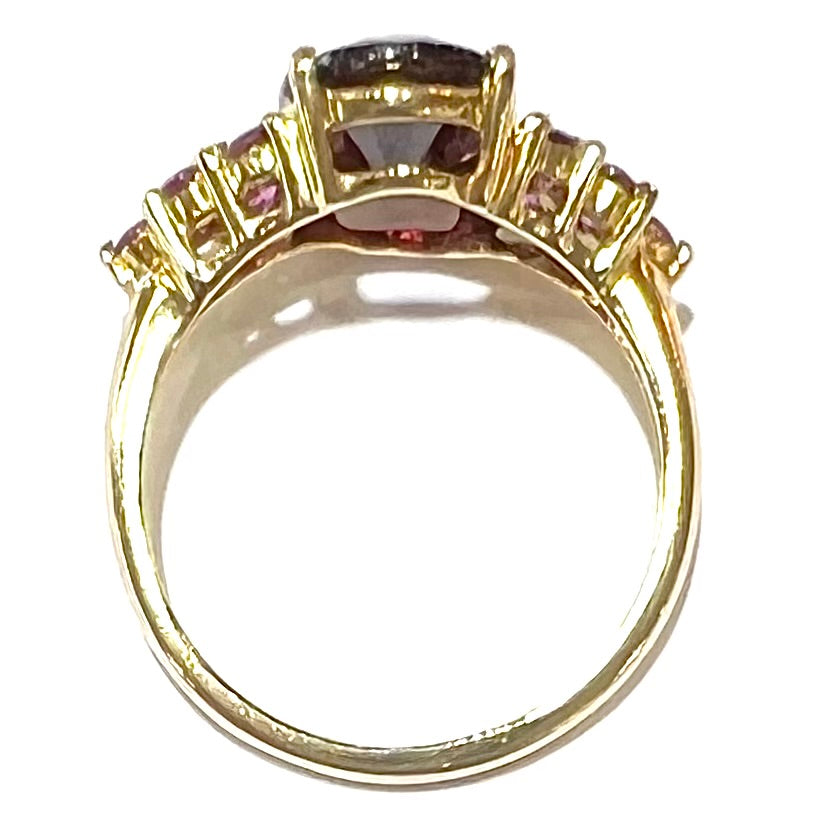 A yellow gold ring set with clusters of purple garnets set on each side of a rhodolite garnet.