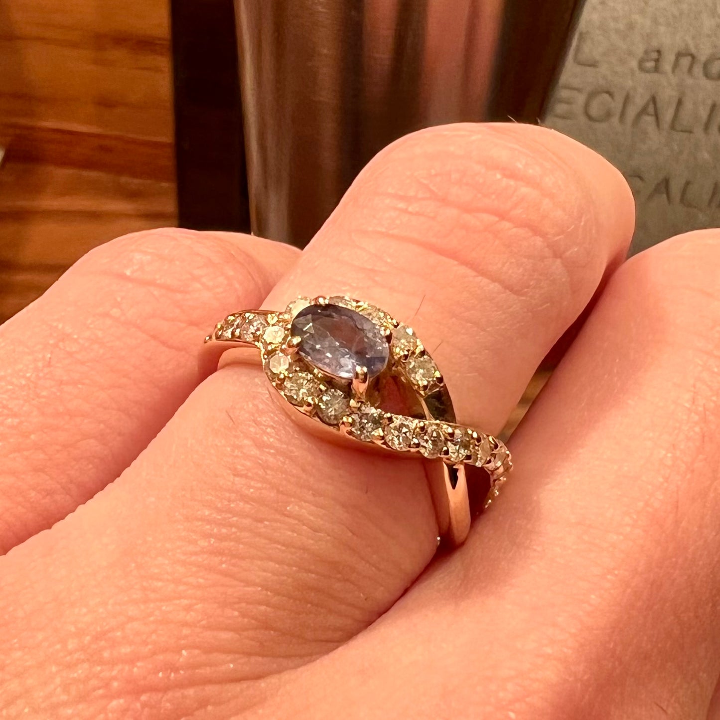 Yellow gold alexandrite and pave set diamond ladies' ring on a hand under orange incandescent light.