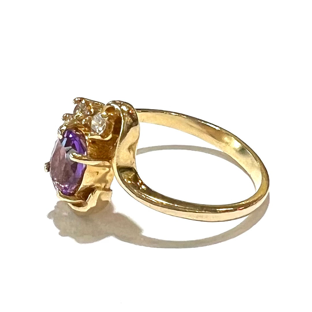 A ring made with 14 karat yellow gold, diamonds, and an amethyst. The ring has a swoosh style.