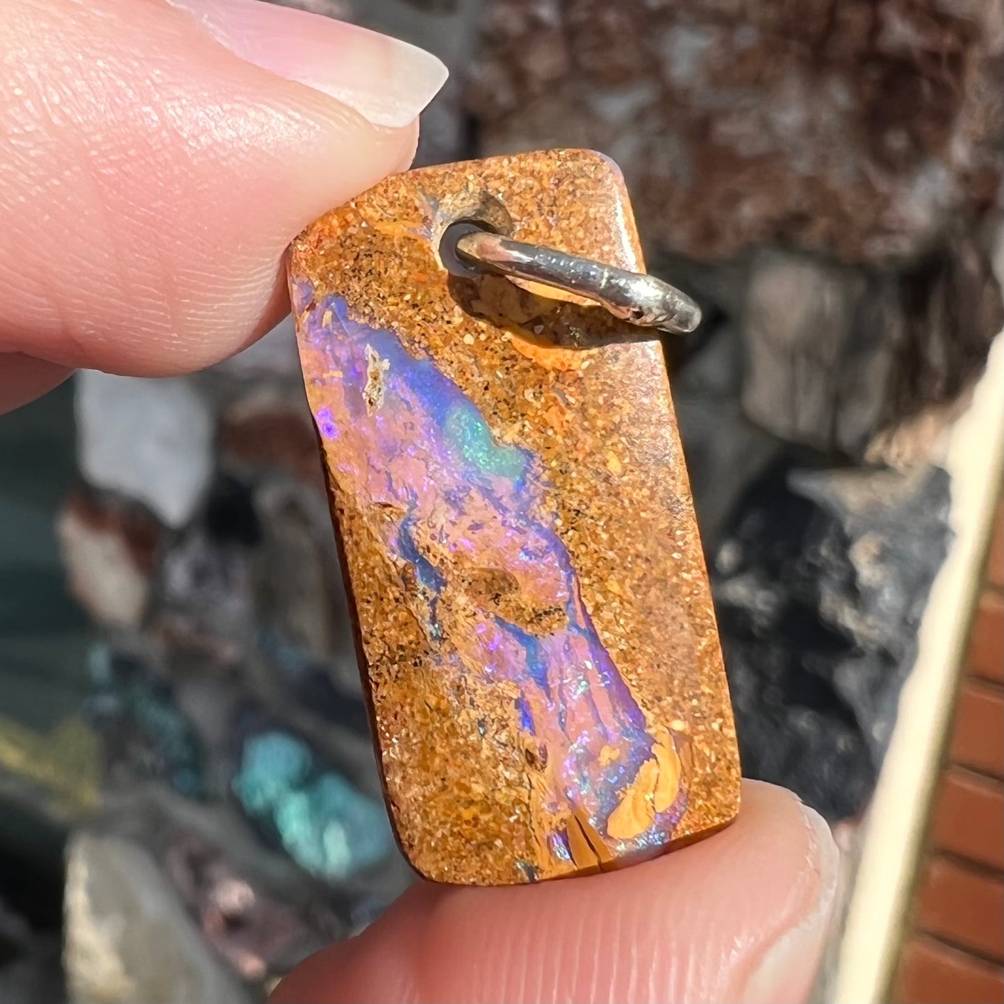 A drilled boulder opal stone with a sterling silver ring through the hole to be worn as a pendant.
