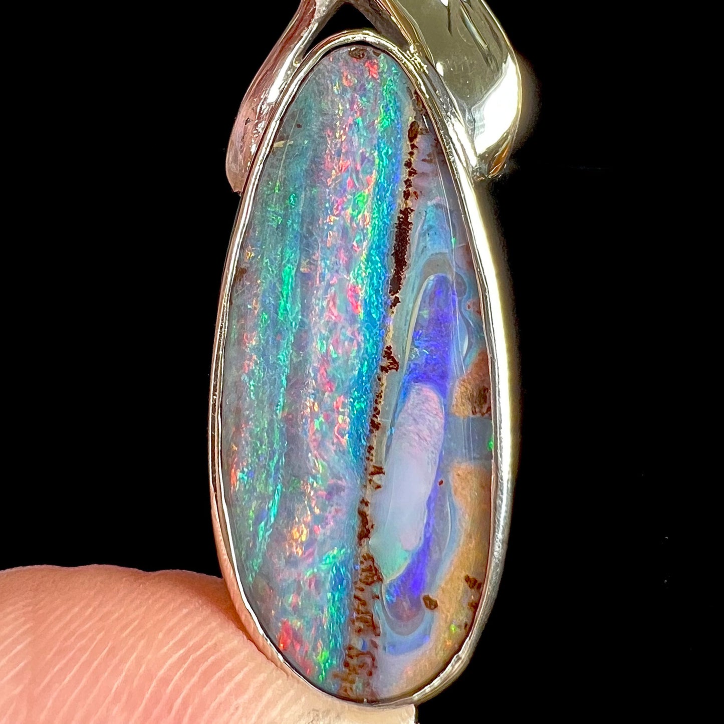 A white gold solitaire pendant set with an Quilpie, Australian boulder opal stone. The opal shines a rainbow of colors.