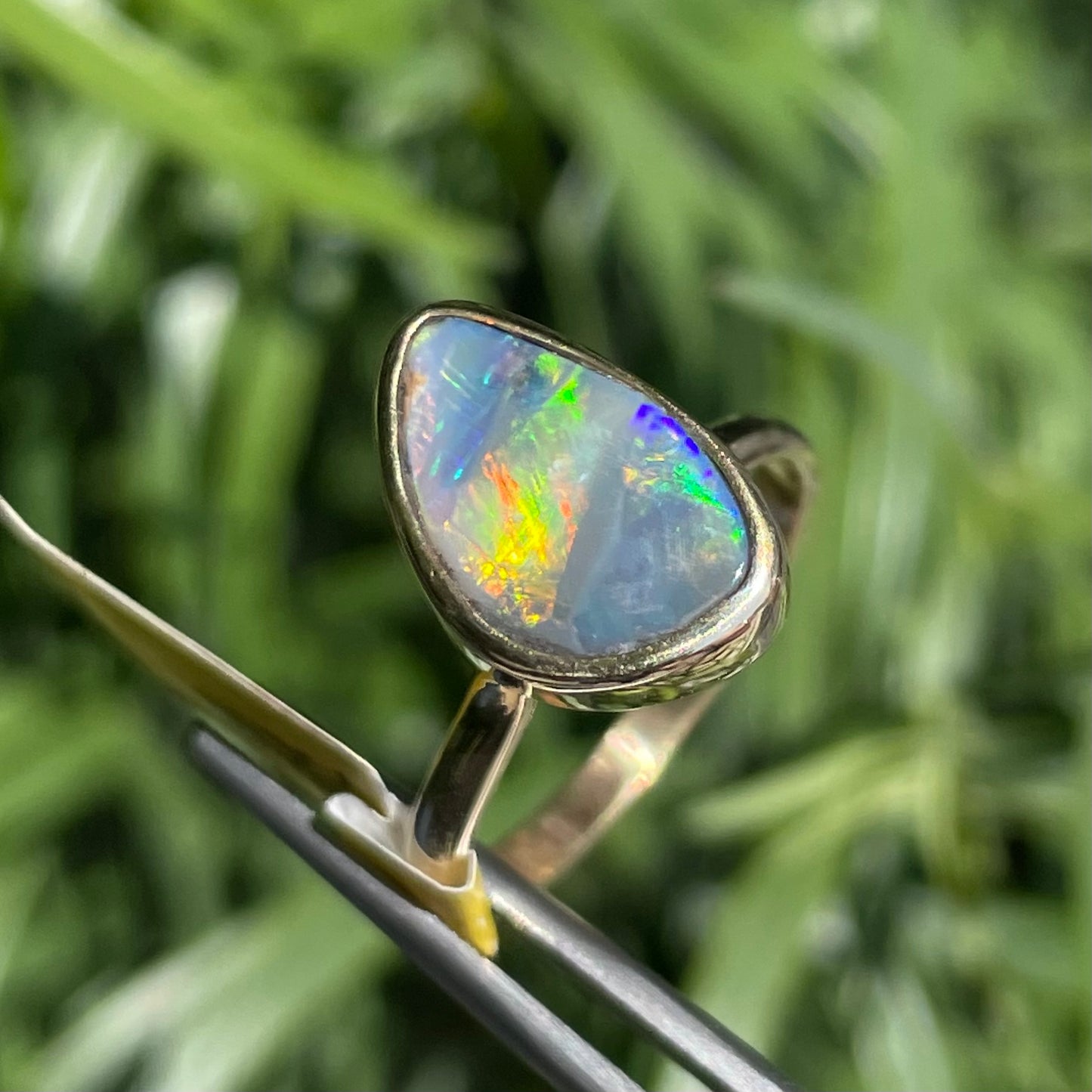 A freeform cut semi-black opal from Lightning Ridge, Australia set in a bezel set yellow gold solitaire ring.