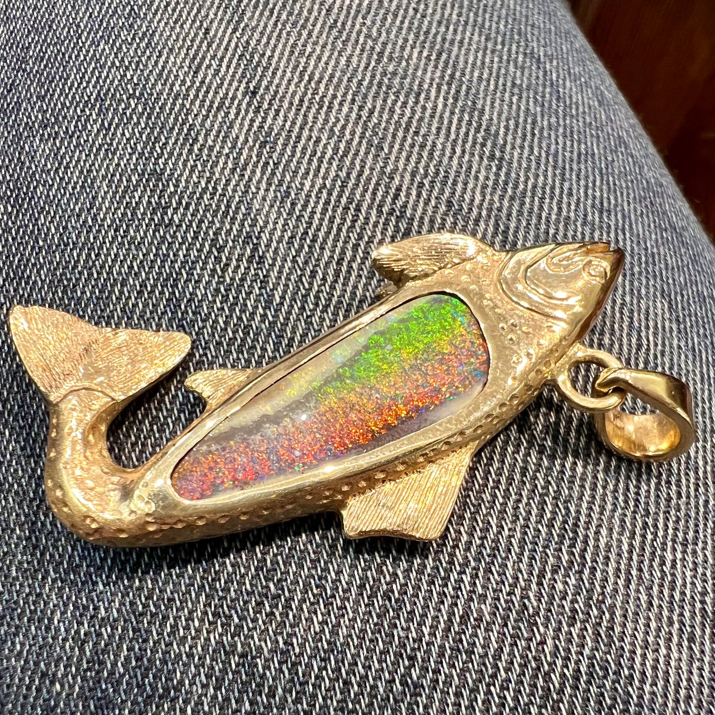 A yellow gold fish pendant detailed to look like a rainbow trout. The body of the fish is set with a color changing black opal stone.