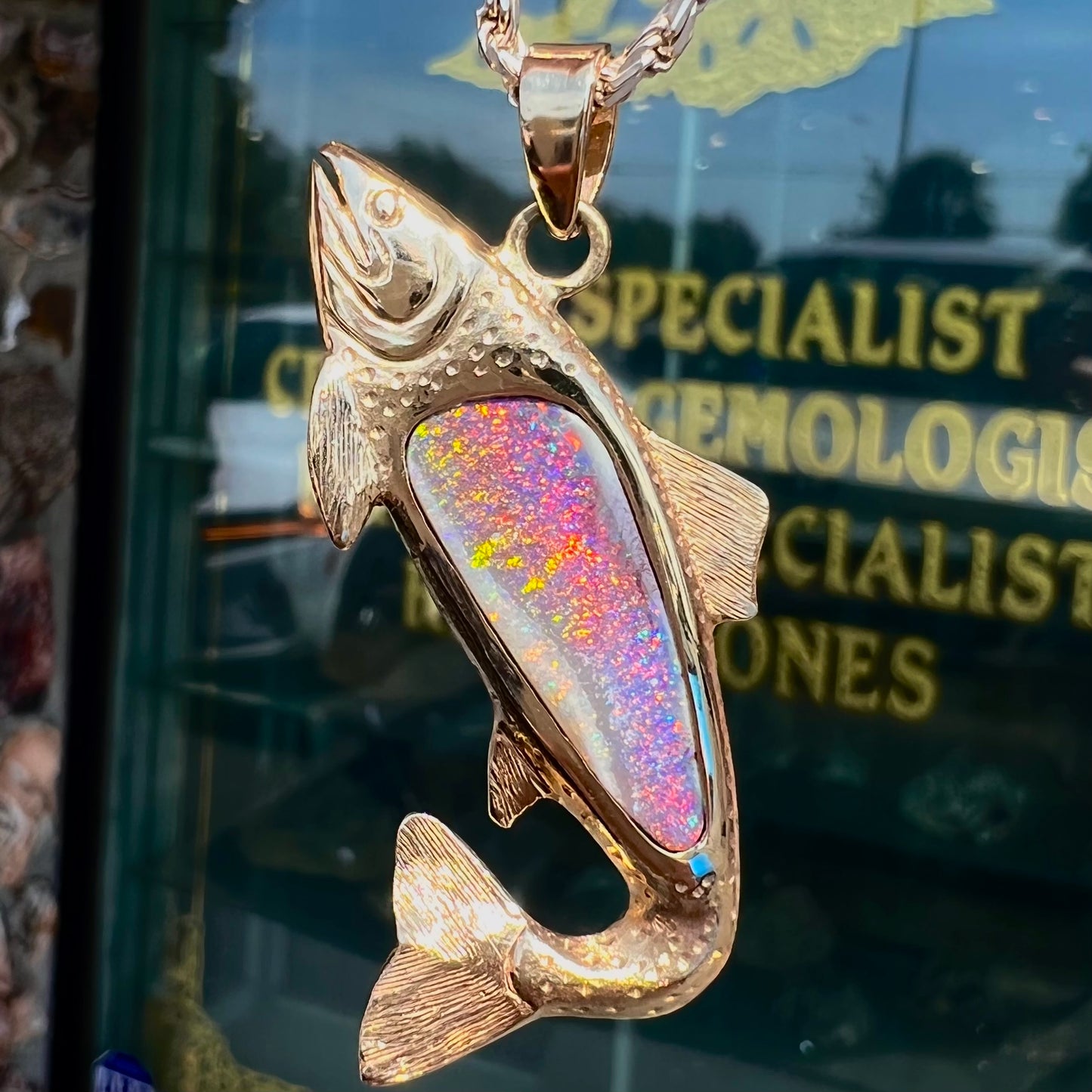 A yellow gold fish pendant detailed to look like a rainbow trout. The body of the fish is set with a color changing black opal stone.