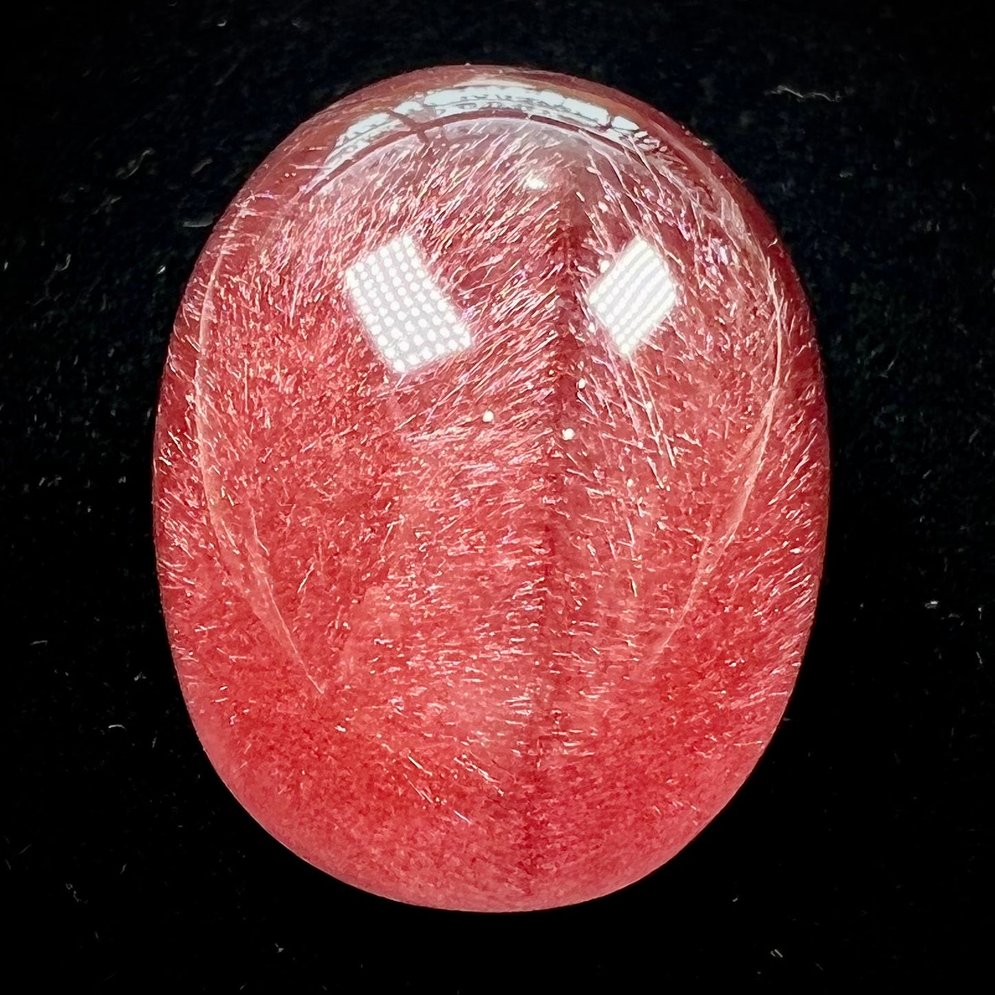 A large, oval cabochon cut strawberry quartz. The stone has a trapiche star-like pattern.