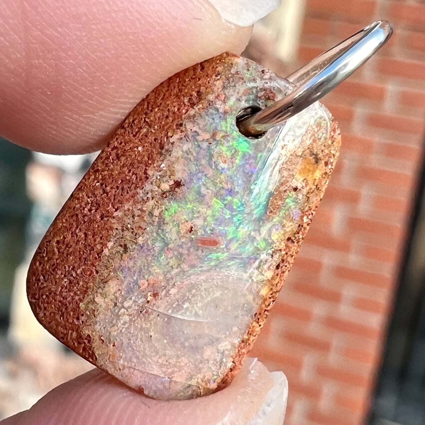 A drilled boulder opal stone with a sterling silver ring through the hole to be worn as a pendant.