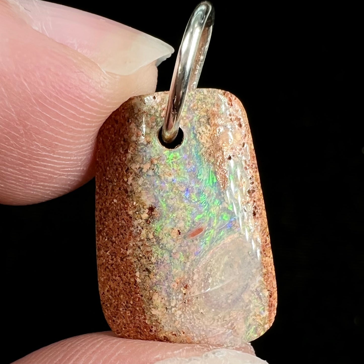 A drilled boulder opal stone with a sterling silver ring through the hole to be worn as a pendant.