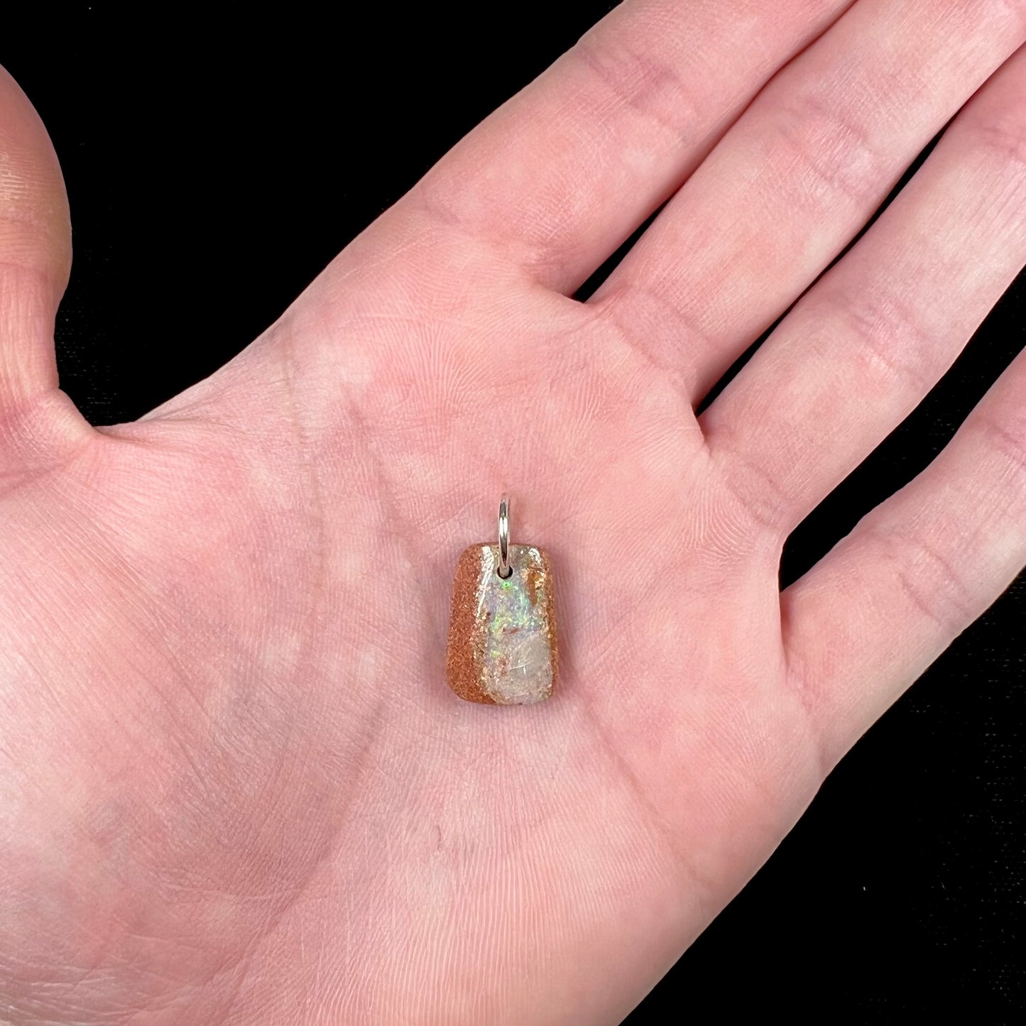 A drilled boulder opal stone with a sterling silver ring through the hole to be worn as a pendant.