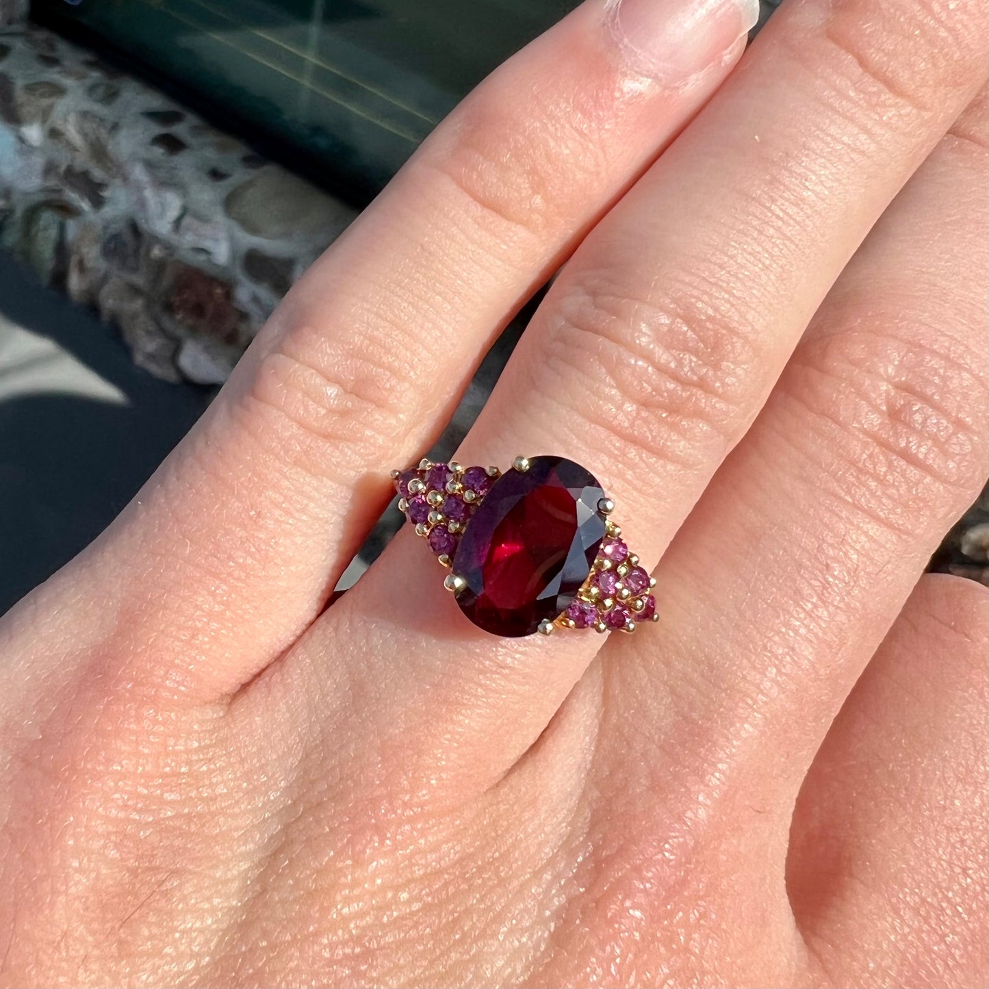 A ring with a crimson reddish purple stone set with clusters of round purple garnets on each side.