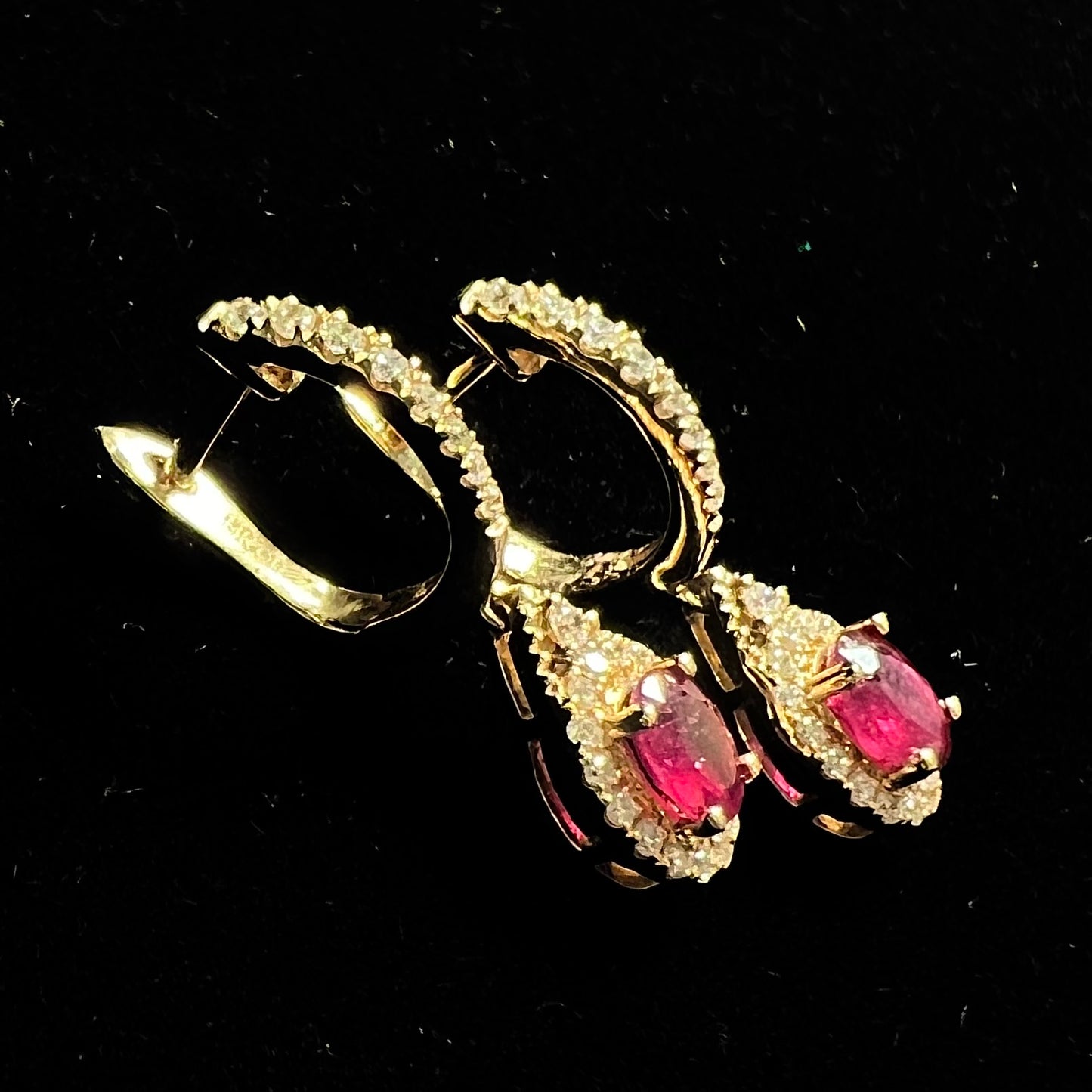 A pair of ruby and diamod halo dangle earrings cast in 14k yellow gold.