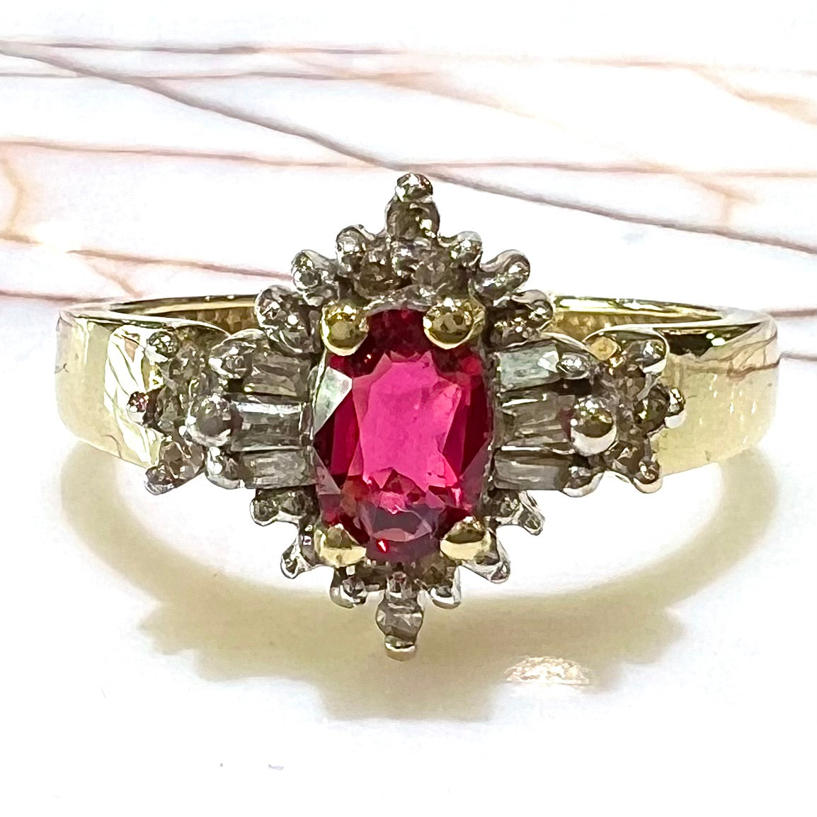 A yellow gold ring set with an oval cut red spinel and diamond rounds and baguettes.