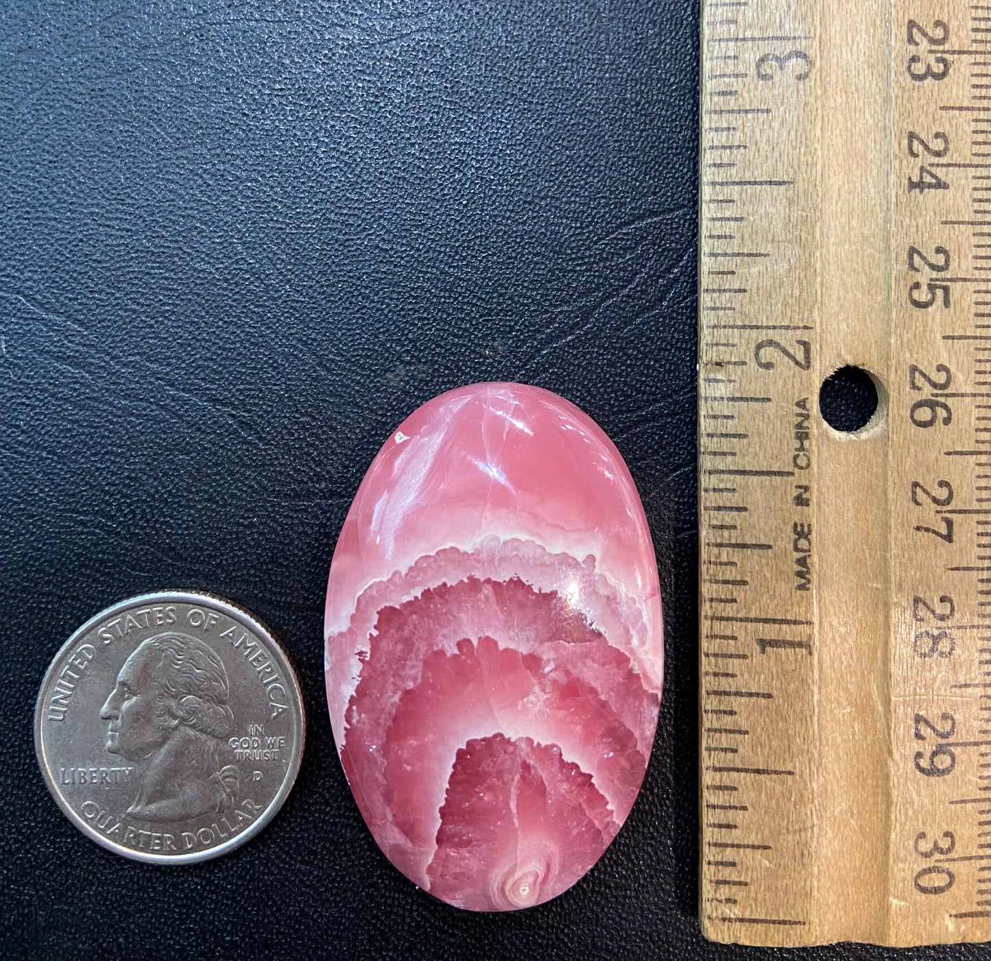 An oval cabochon cut pink rhodochrosite stone.