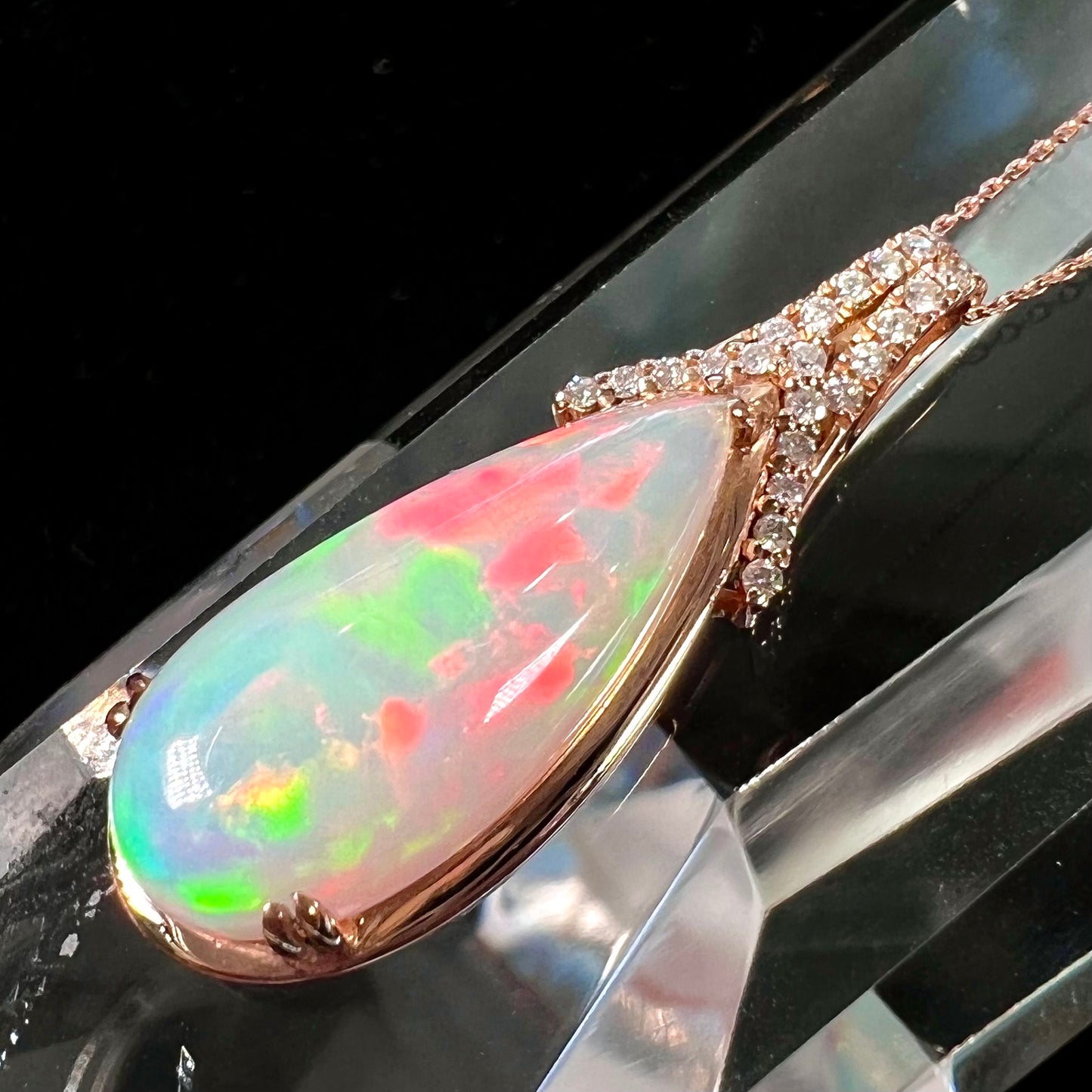 A rose gold, teardrop shaped fire opal and diamond necklace on a cable chain.