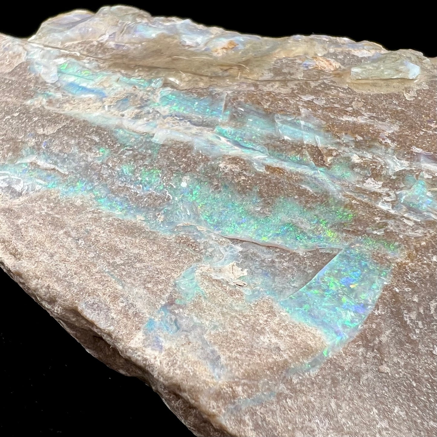 A rough Painted Lady boulder opal specimen that shows blue, green, and pinkish red colors.