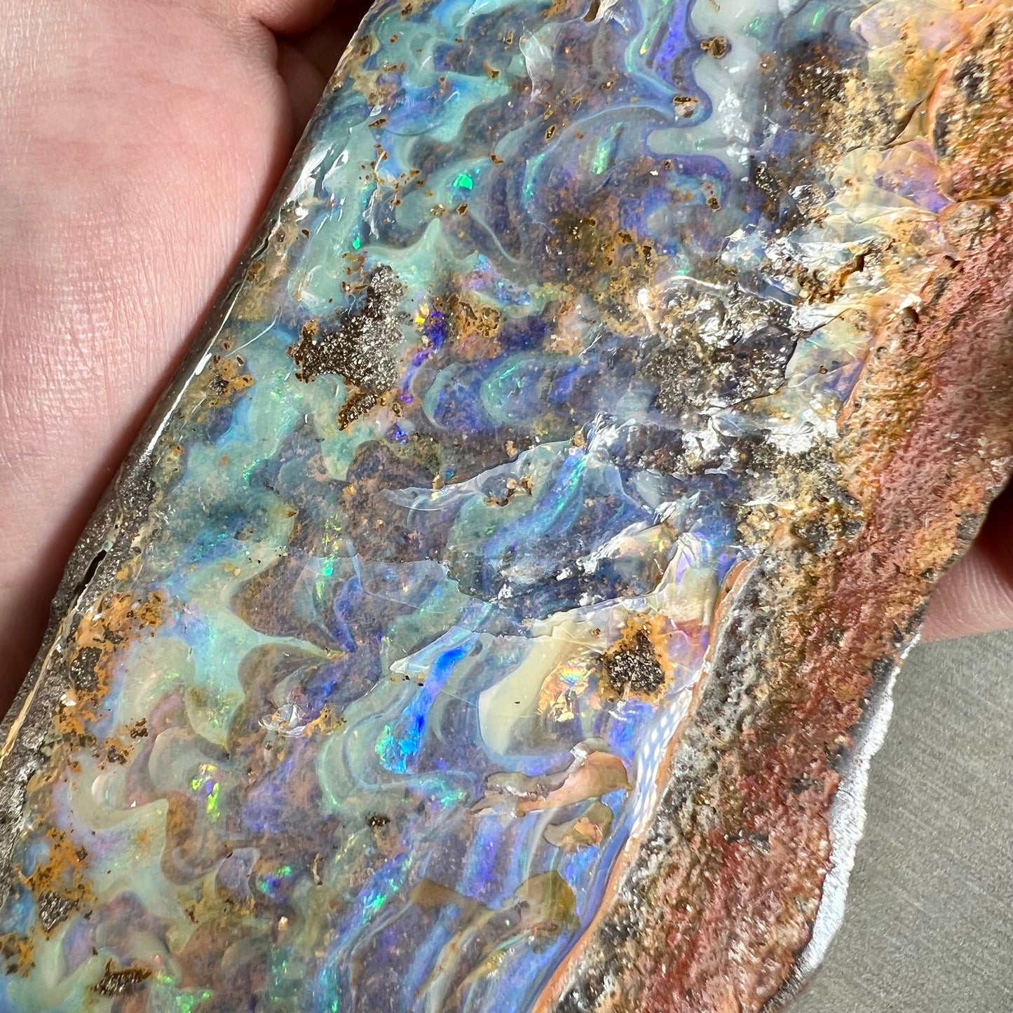A 7 inch long, polished Quilpie boulder opal specimen. The stone shows colors of blue, green, and orange.