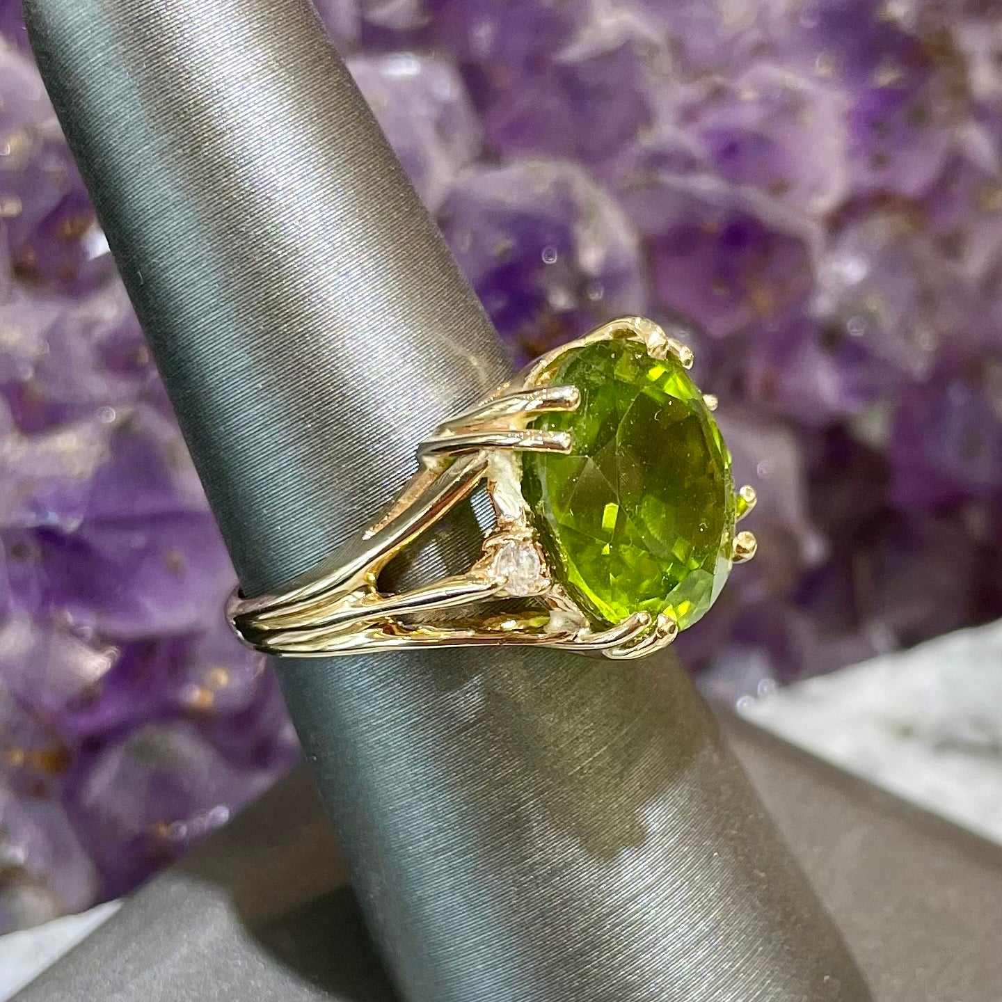 A ladies' round brilliant cut peridot statement ring set with two round diamond accents in yellow gold.