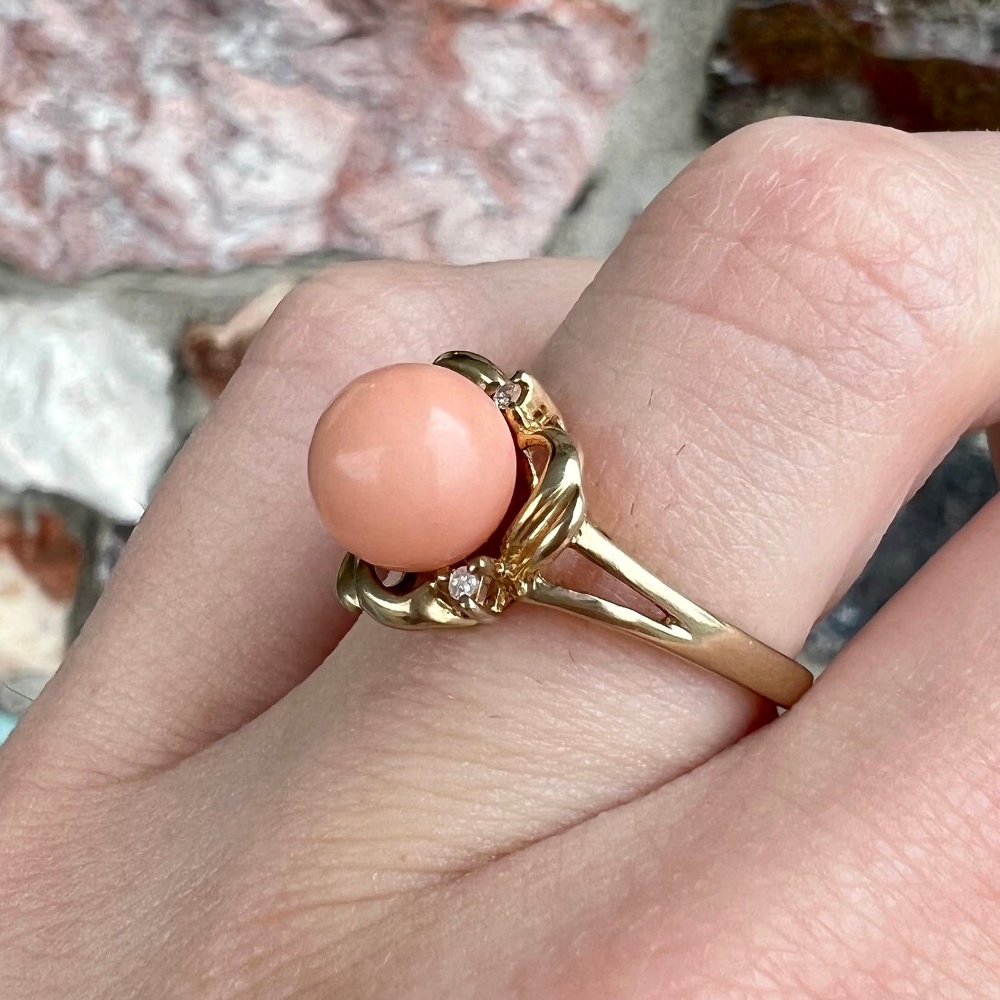 A vintage split shank flower ring set with a round pink coral sphere and diamond accents.