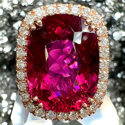 A rose gold, split shank engagement ring set with a cushion cut rubellite tourmaline in a diamond halo.